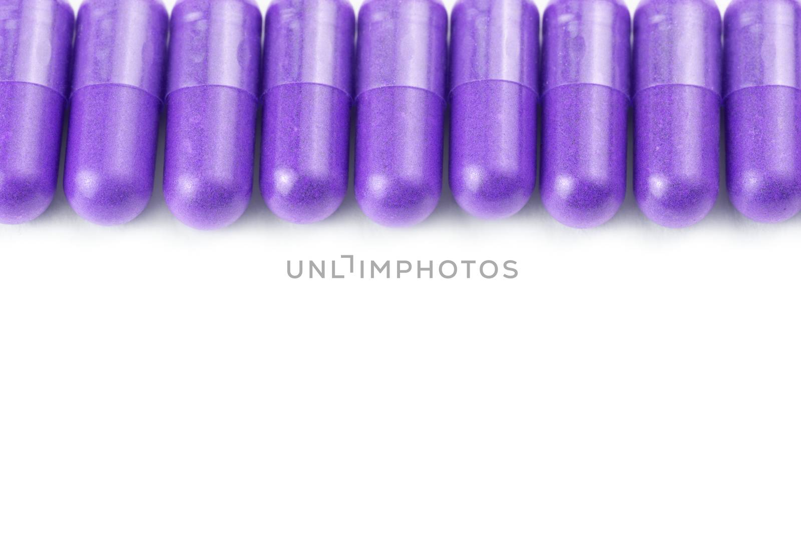 row of proton purple color organic capsules isolated on white background closeup with selective focus.