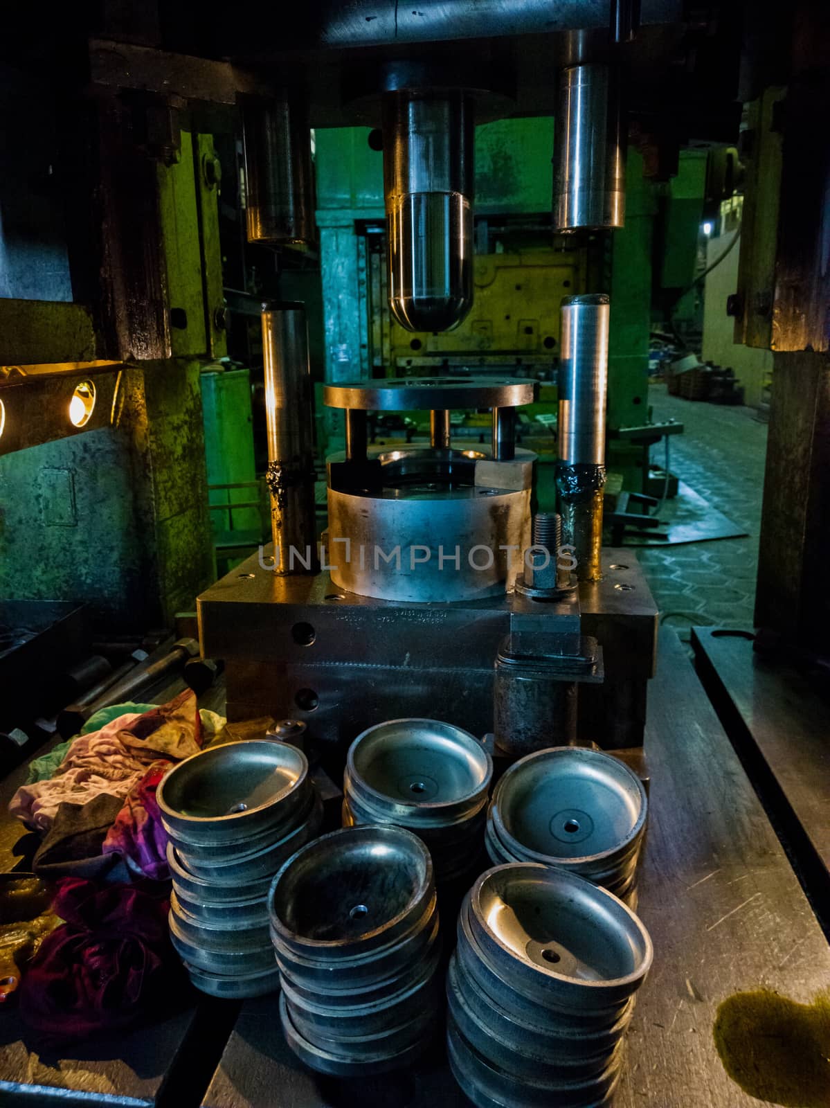 dirty used low tech stamping press producing round aliminium parts in dark environment.