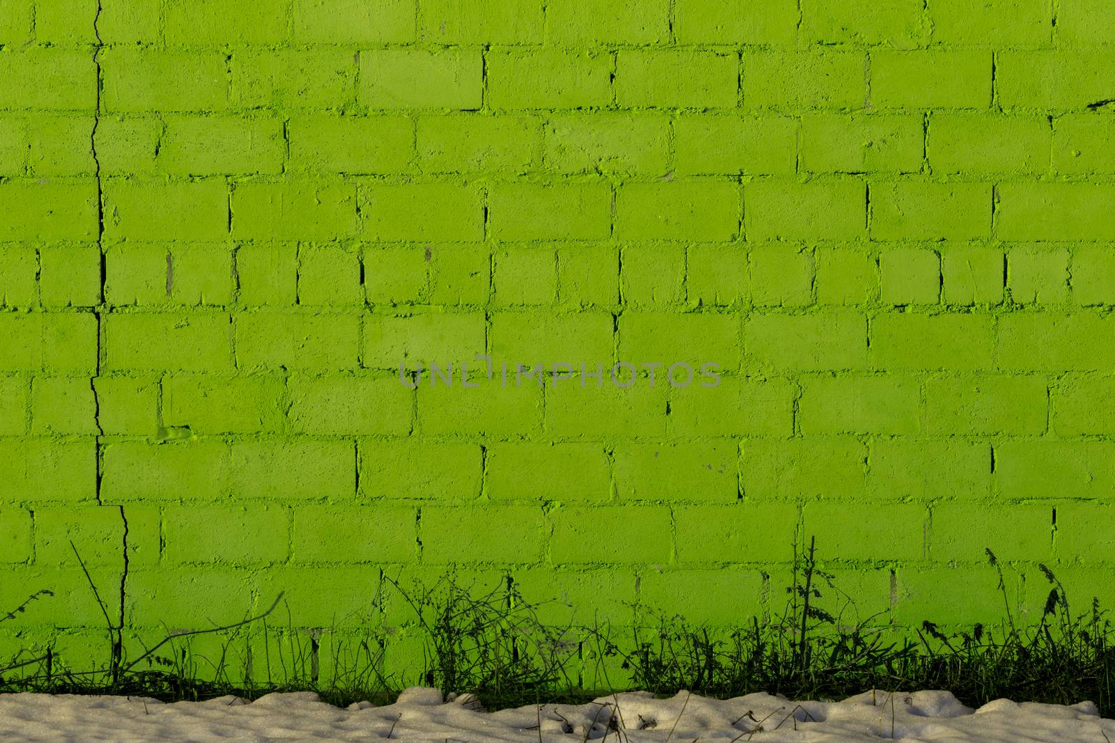 green plaster rough brick wall texture under direct sunlight with snow and dry gasss under
