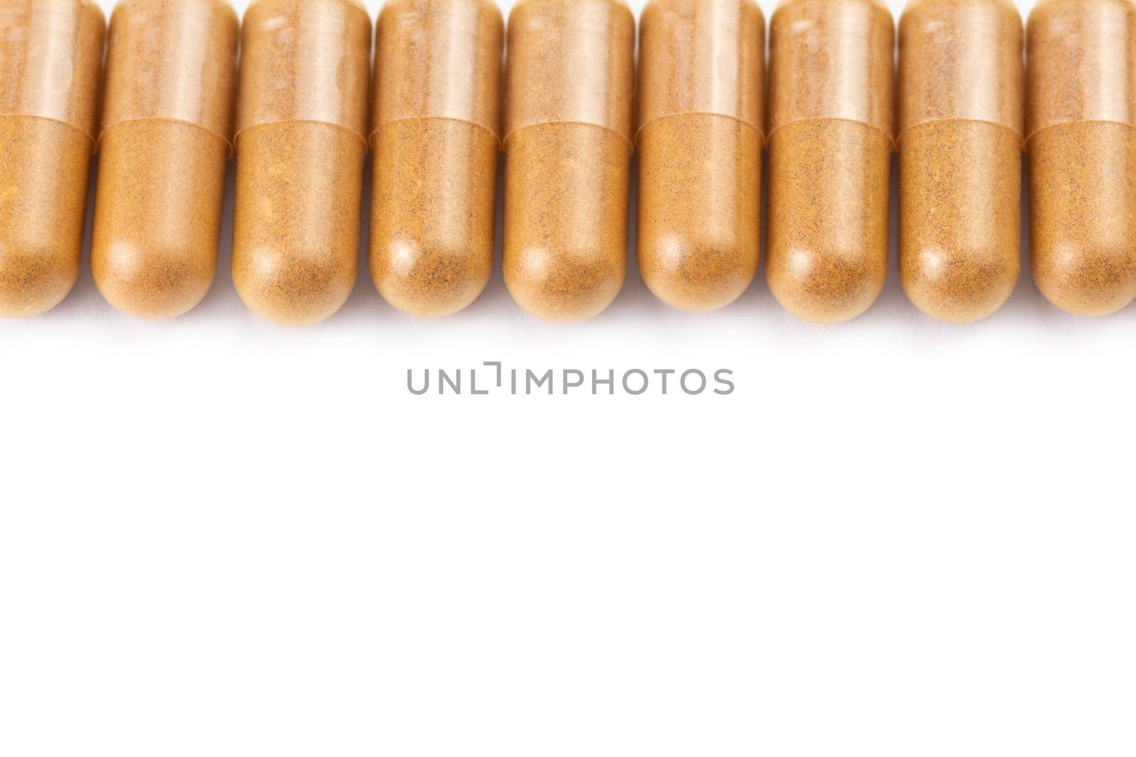 row of orange color organic capsules isolated on white background closeup with selective focus.
