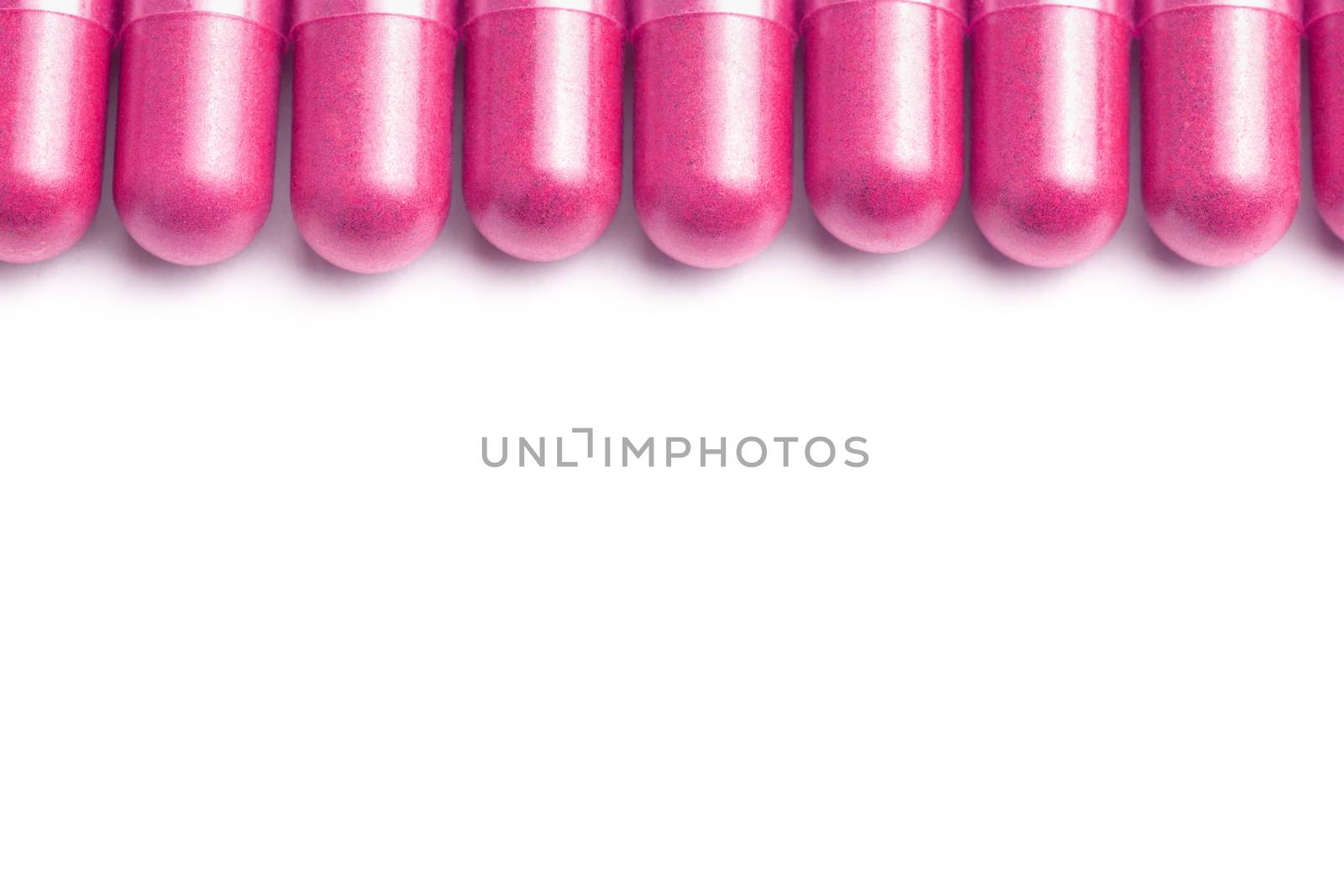 row of plastic pink color organic capsules isolated on white background closeup with selective focus.