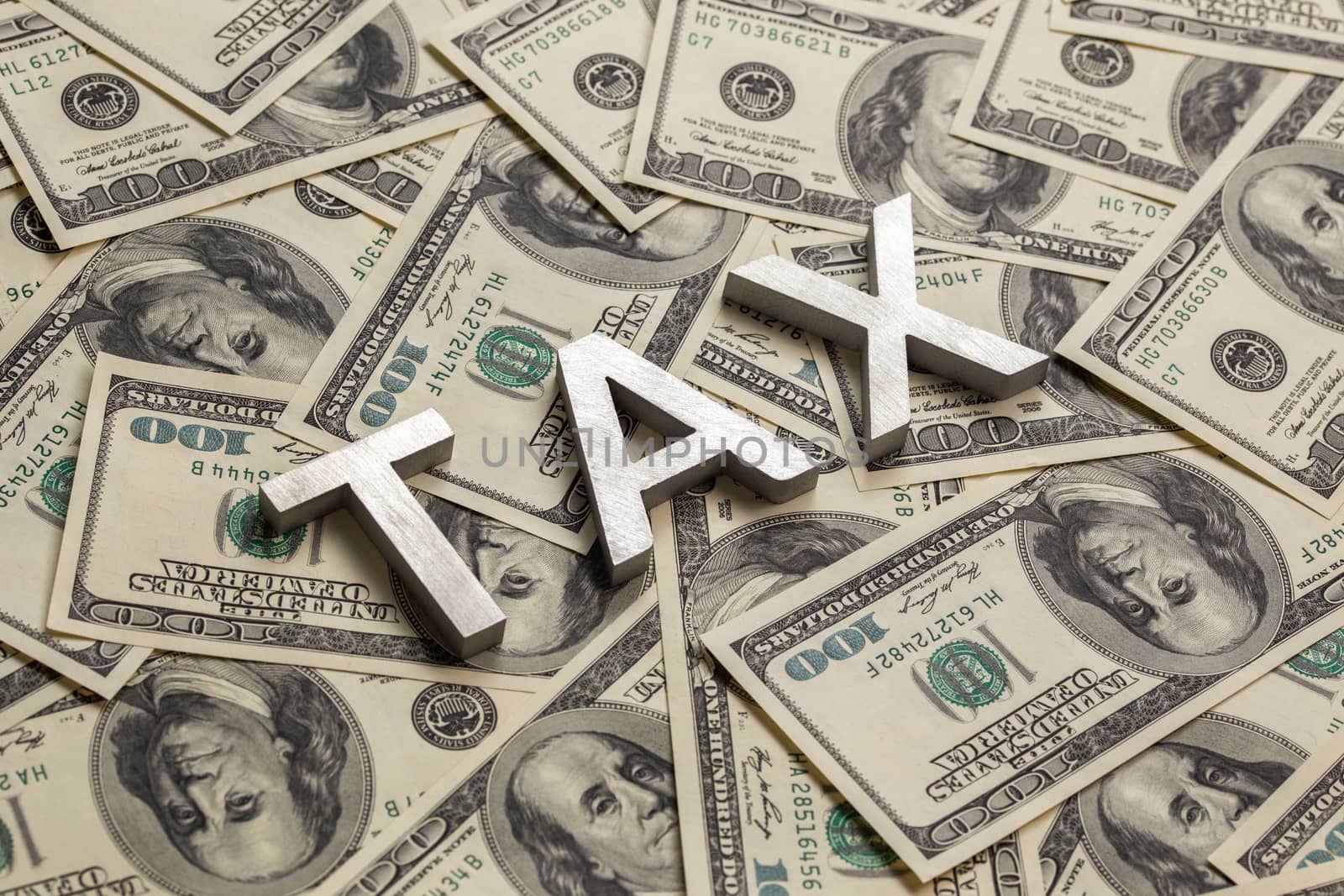The words TAX laid with aluminium thick letters on the US dollar bills background - with selective focus and diagonal composition.