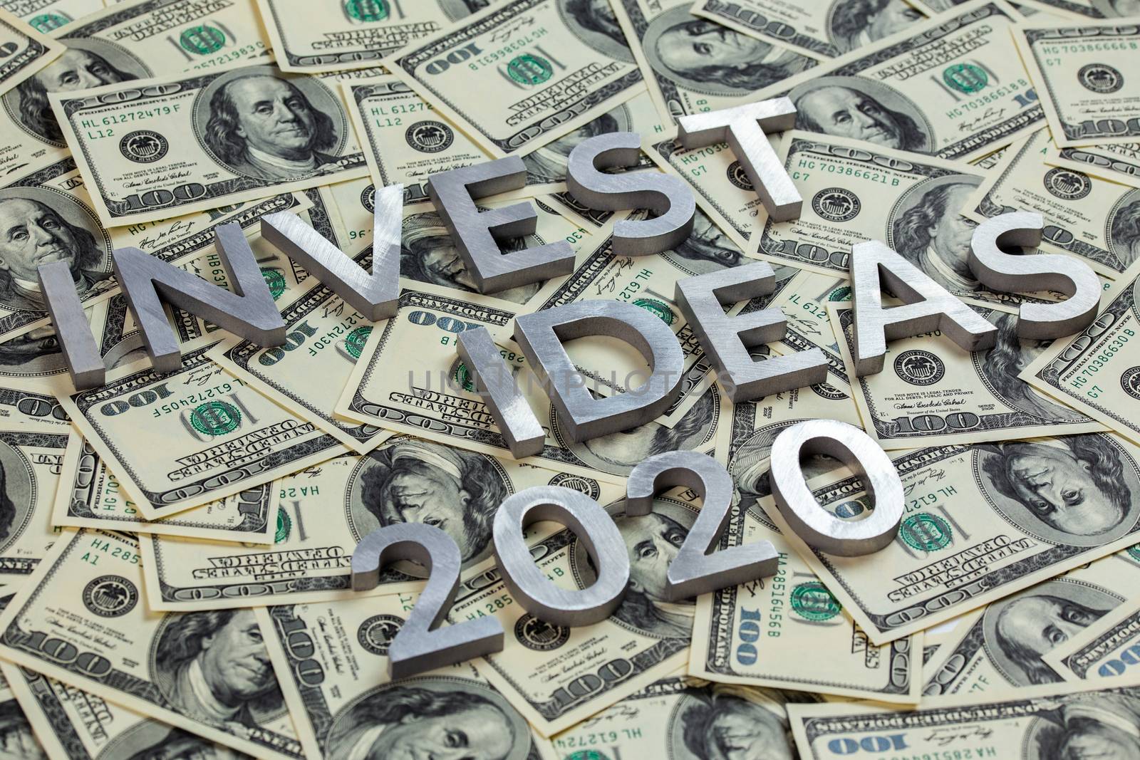 The words INVEST IDEAS 2020 laid with metal letters on the US dollar bills background - with selective focus and diagonal composition.