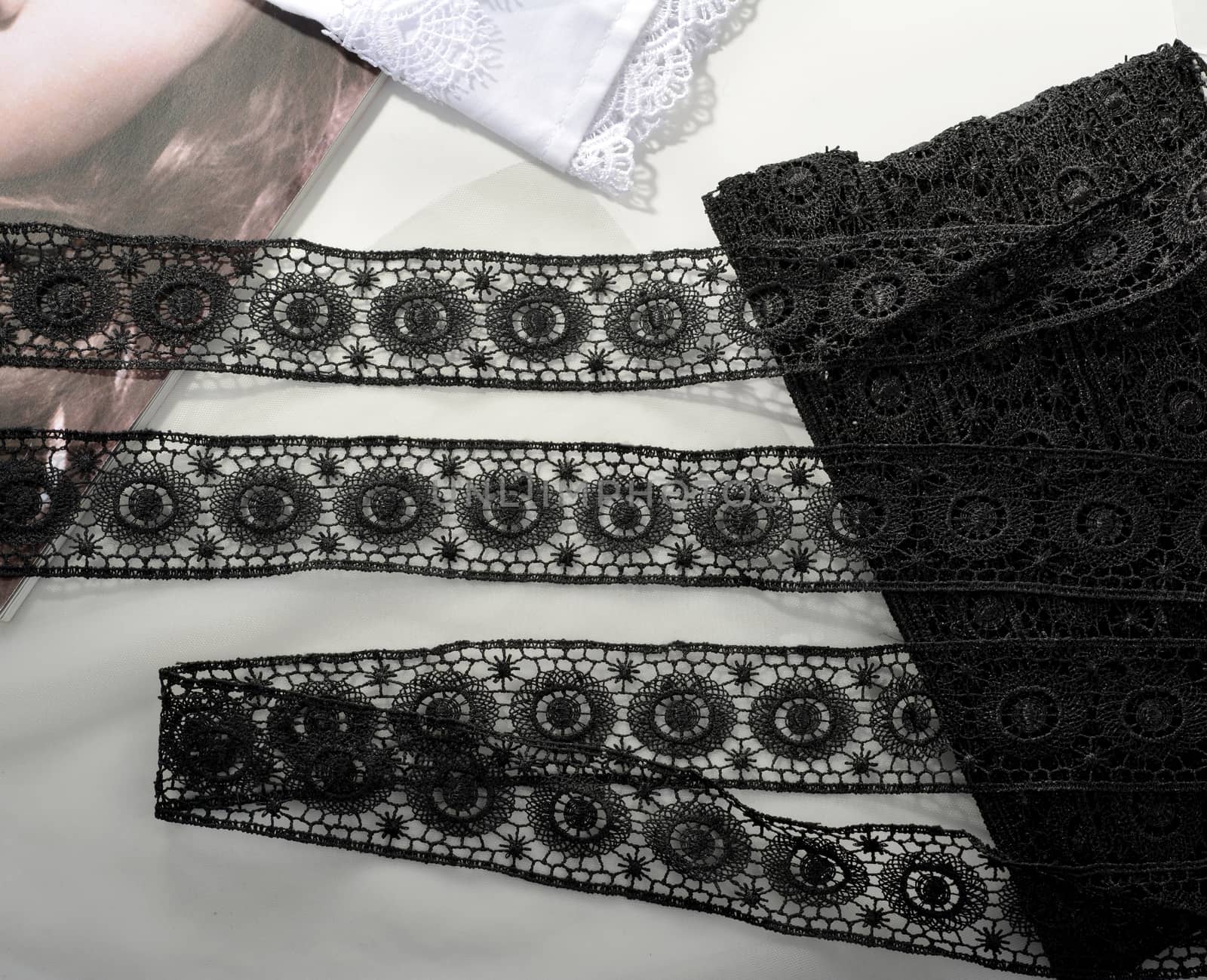 Tapes of black gentle guipure, beauty lace fabric on light background. Elastic material. Using for Atelier and needlework store.