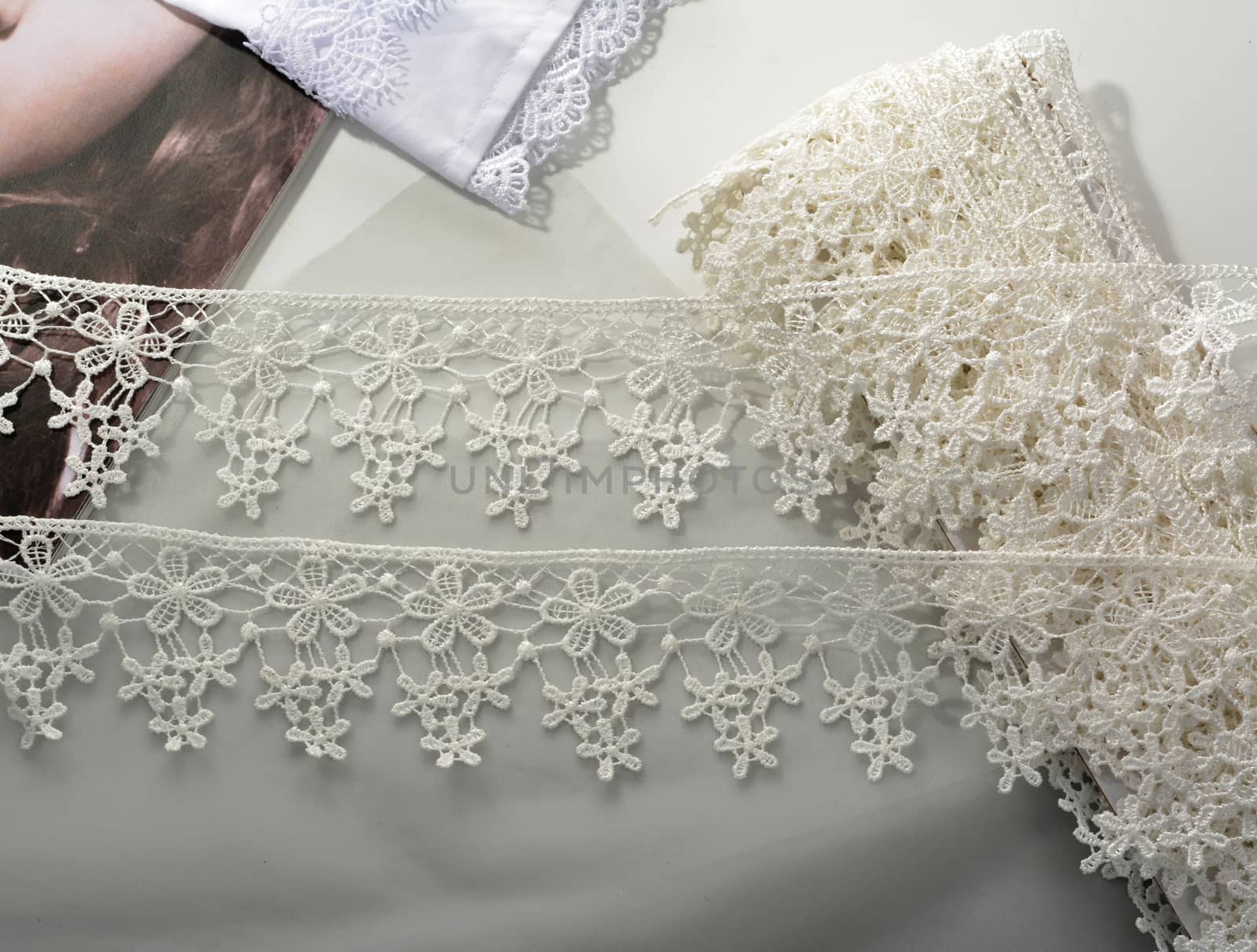 Tapes of ecru white guipure, beauty silk lace fabric on light background. Elastic material. Using for Atelier and needlework store. Flat lay style