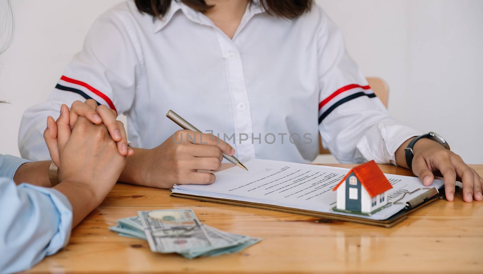 Cropped image of real estate agent assisting client to sign contract paper at desk with house model.