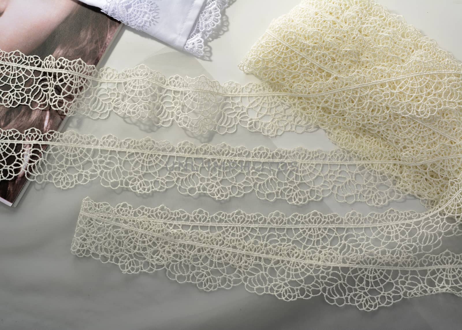 Tapes of ecru white guipure, beauty silk lace fabric on light background. by polyats