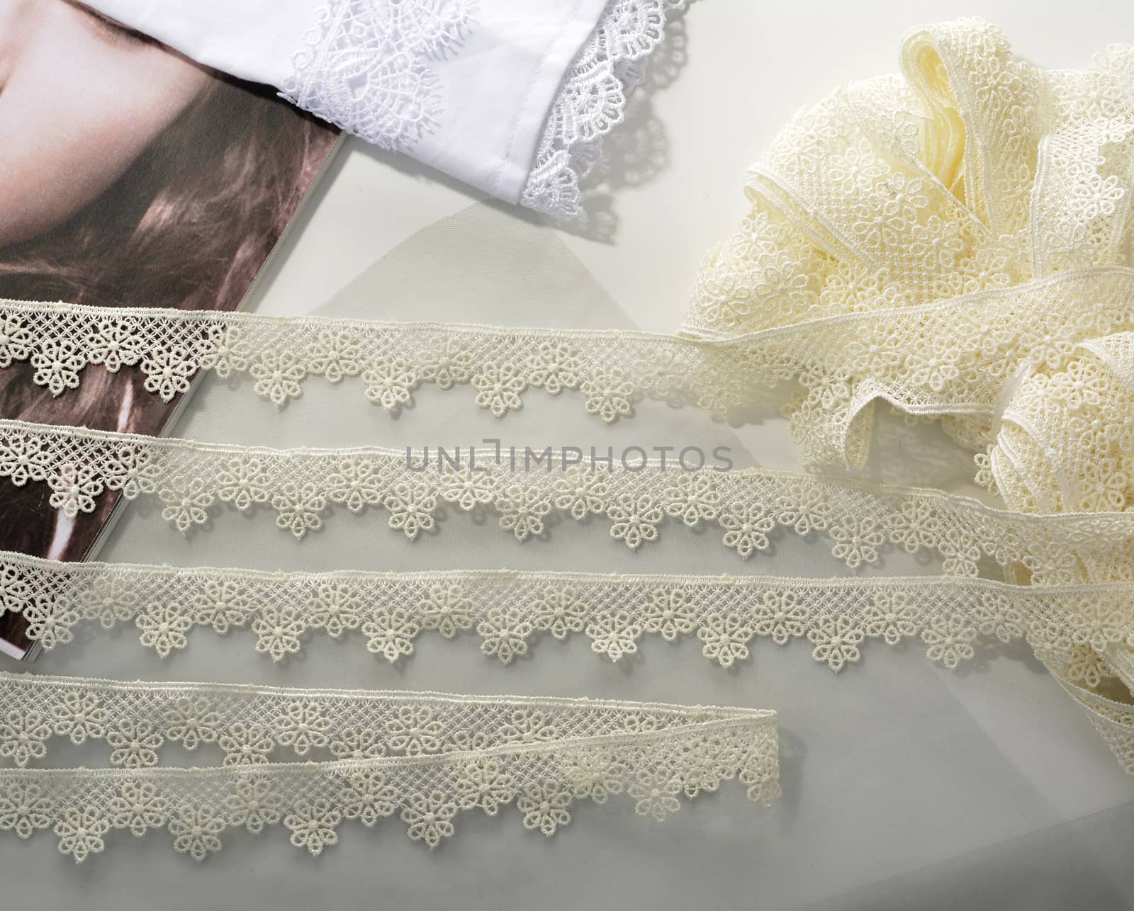 Tapes of ecru white guipure, beauty silk lace fabric on light background. by polyats