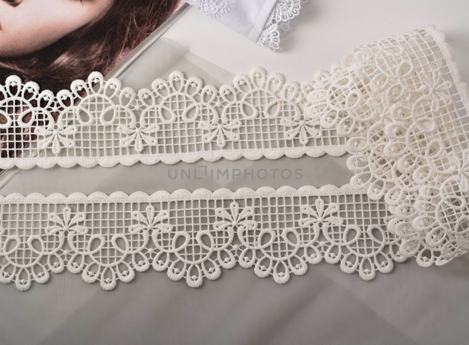 Tapes of ecru white guipure, beauty silk lace fabric on light background. by polyats