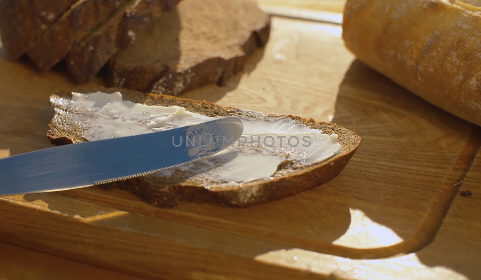 Close up hand smearing bread with butter on a wooden cutting board