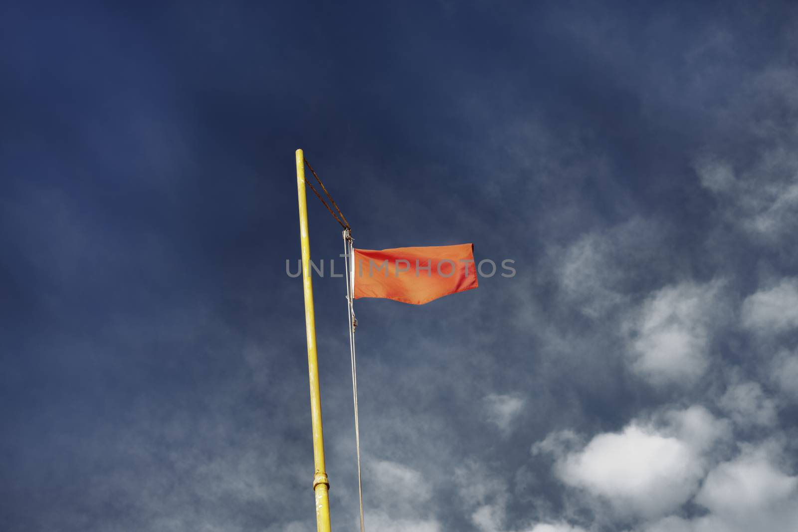 Red warning flag on a yellow flagpole against a blue and cloudy sky  seen from below