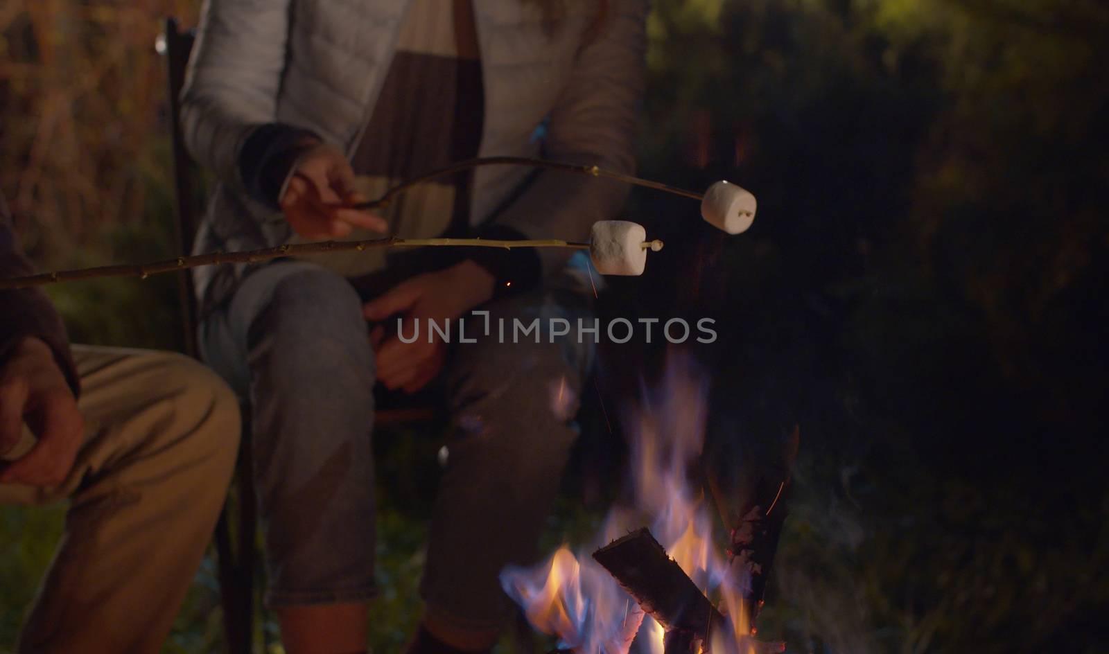 Close up bonfire. Young happy couple at night roasting marshmallow on campfire. Family on weekend in the forest. Healthy lifestyle concept