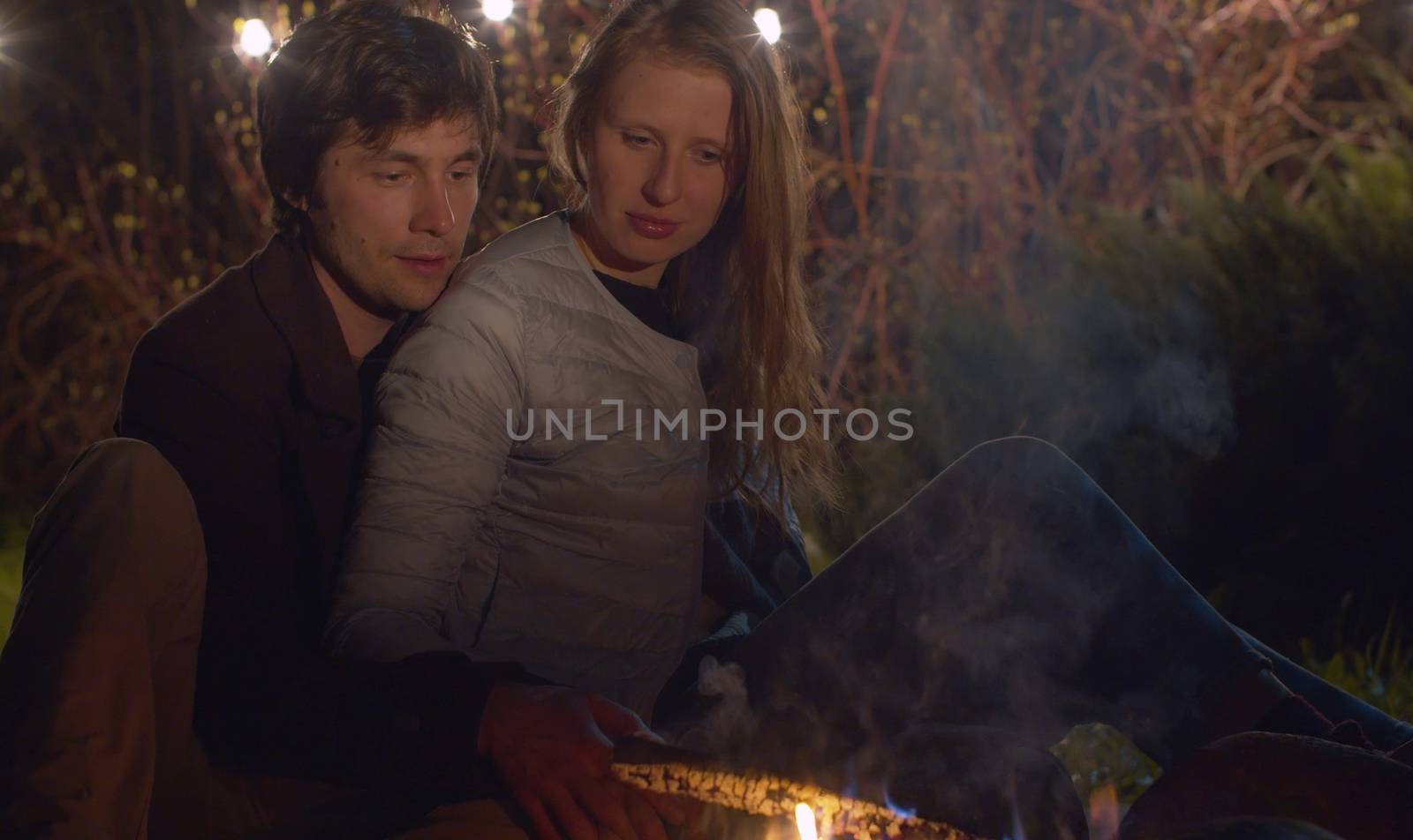 Young happy family at night sitting near bonfire and hugging. Couple on weekend in the forest. Healthy lifestyle concept