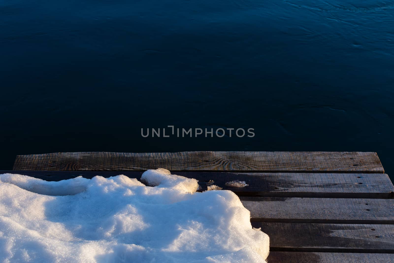 wooden pier with snow on dark water background.