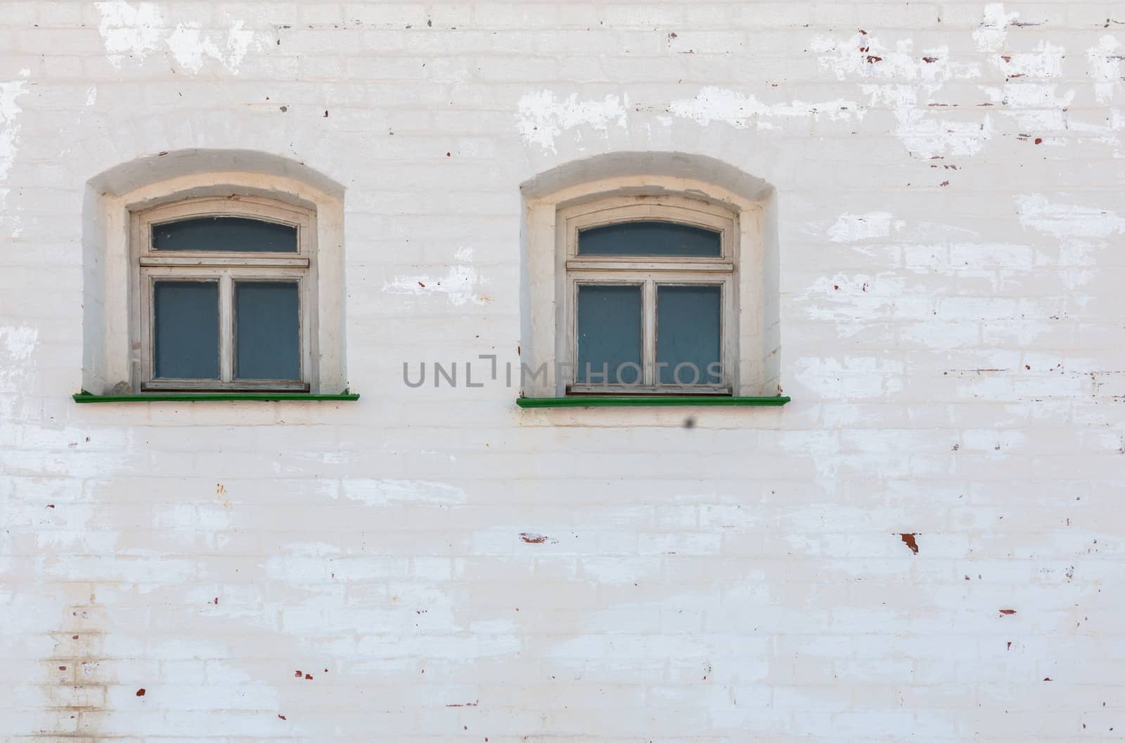 two windows in thick brick mediewal wall under worn layer of white plaster.