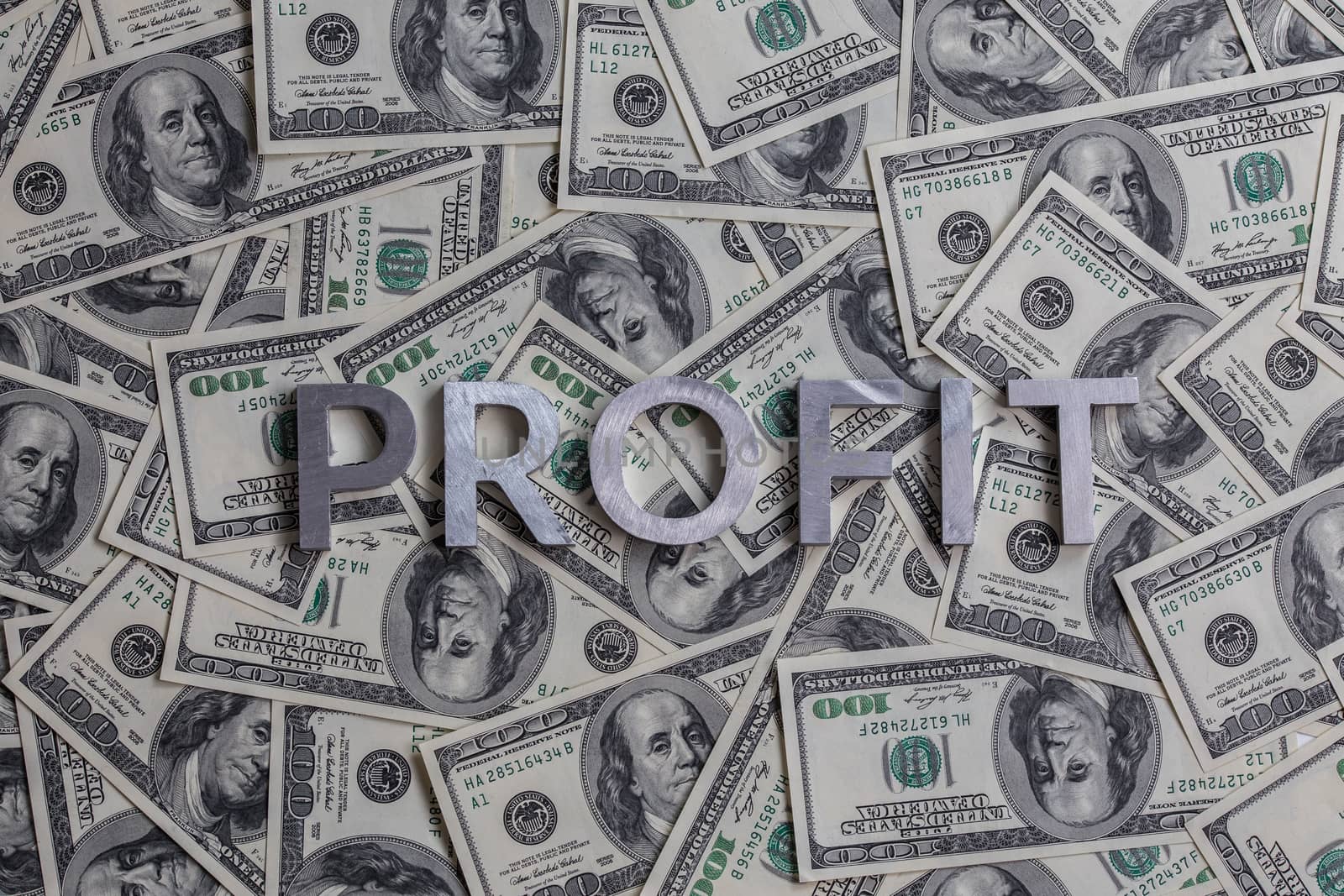 The word PROFIT laid with aluminium letters on the US dollar banknotes background - with selective focus.
