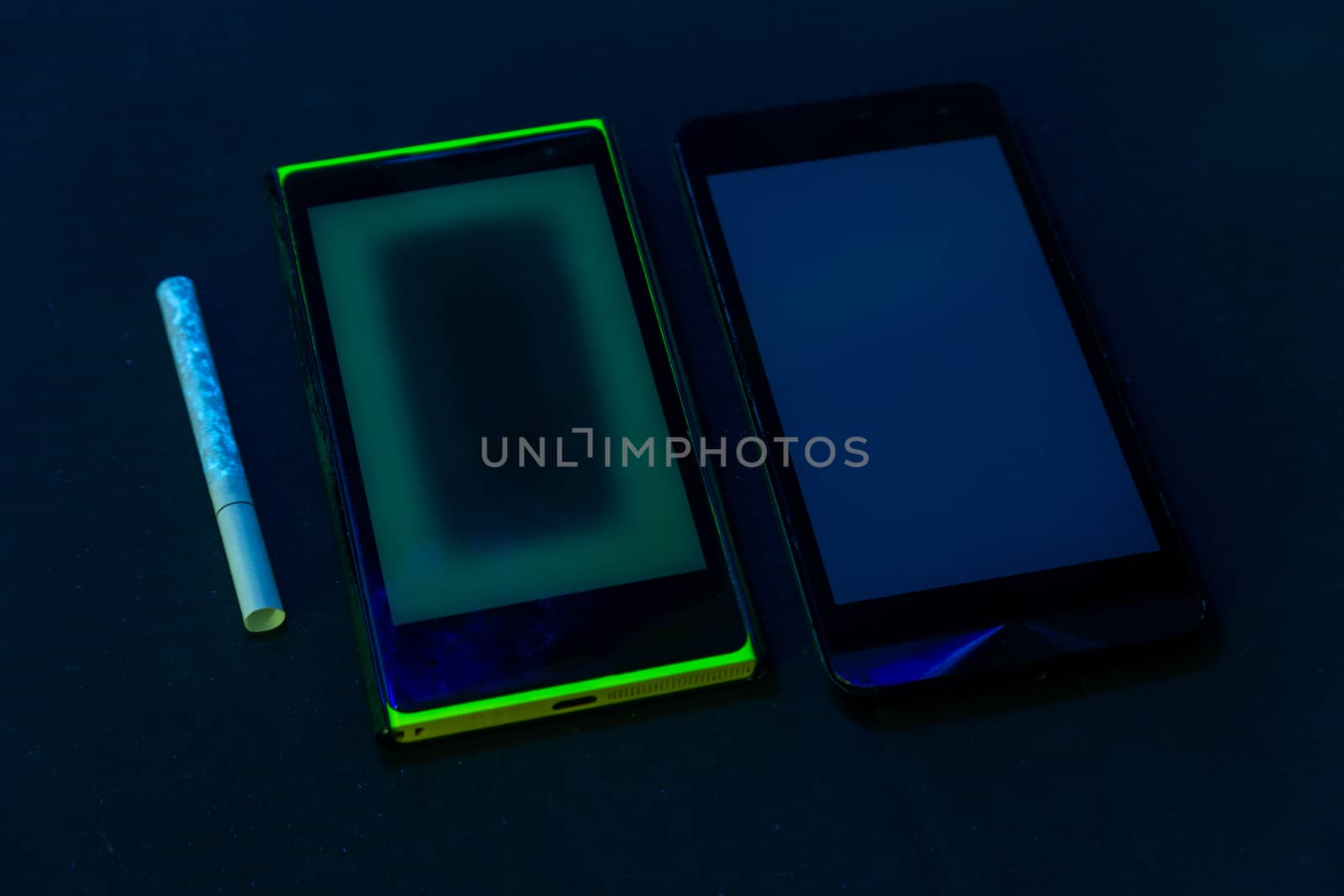 used phones and cigarette under UV light on black bckground with selective focus.