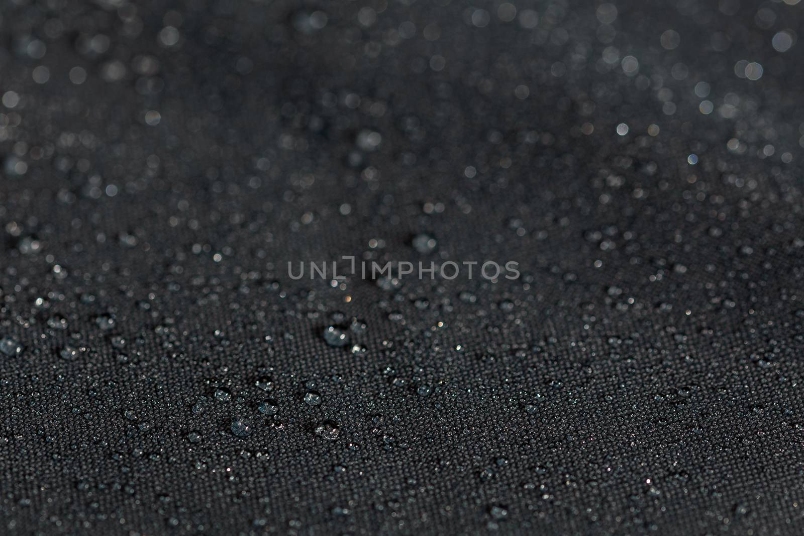 dark gray waterproof hydrophobic flat cloth closeup with water drops selective focus background.