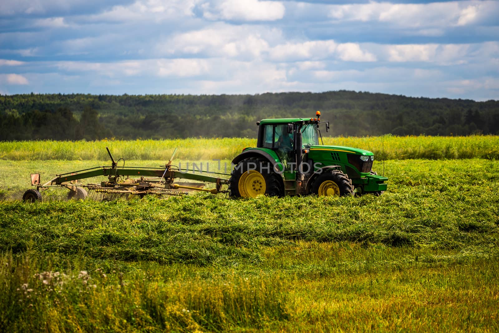 green haymaking tractor on summer field before storm - telephoto shot with selective focus and blur.