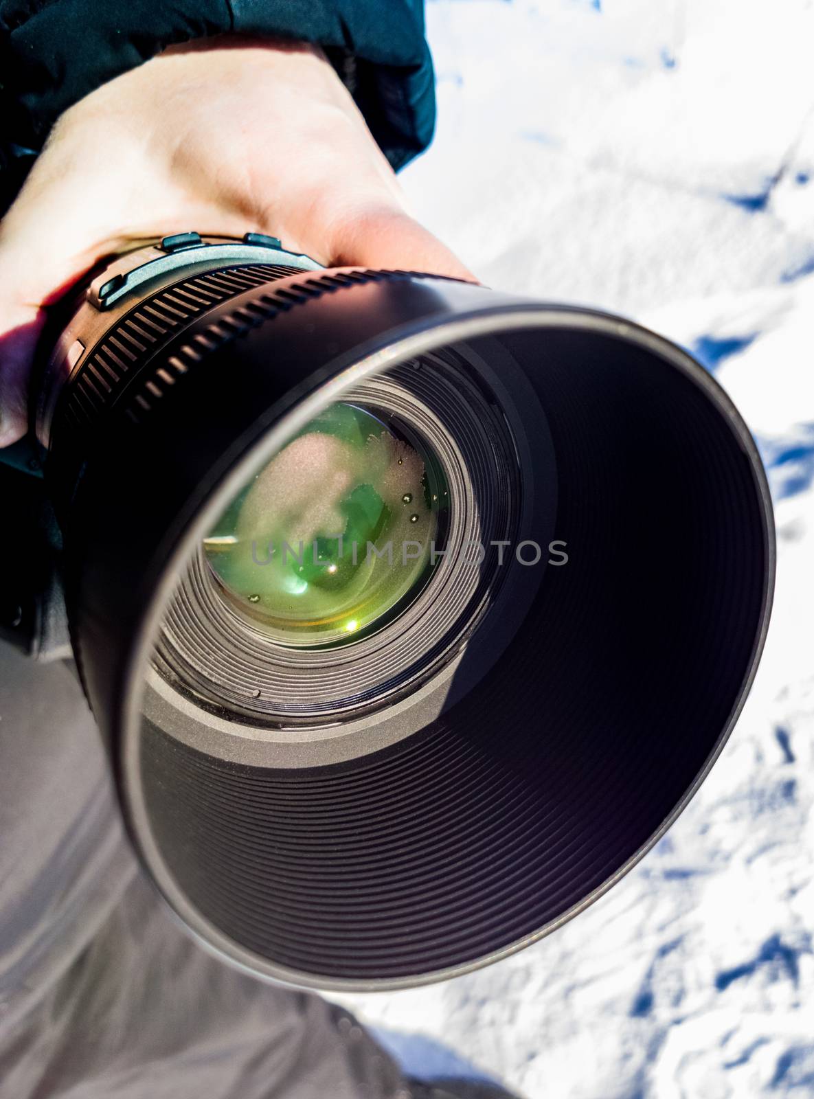 A telephoto dslr camera lens with dew sweating and snow at outdoor winter photoshoot. Real life situation with part of hand, holding camera.
