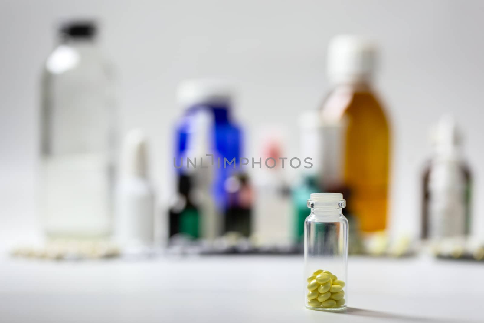 Small glass bottle with yellow gloss tablets on blurred meds background with selective focus .