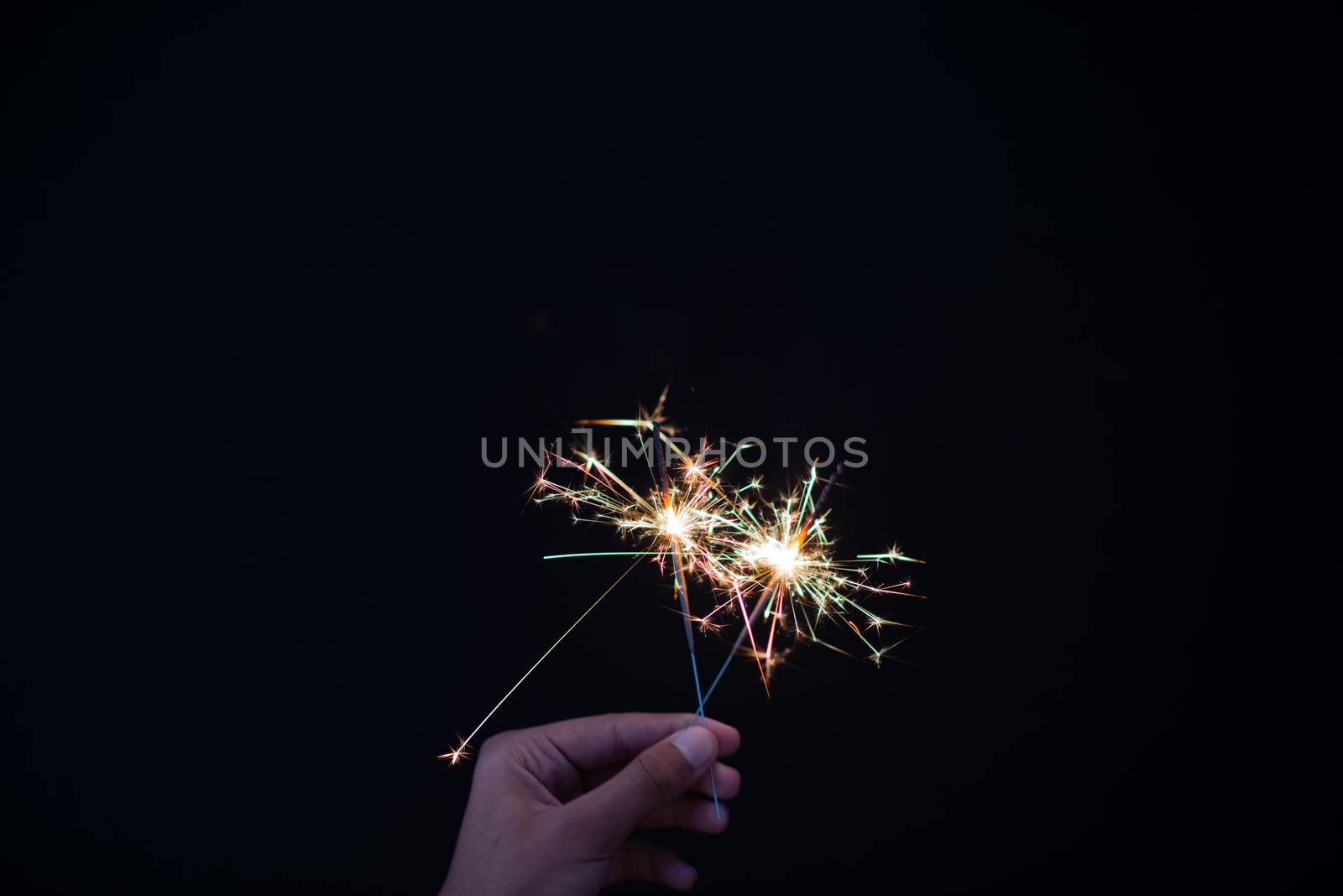 Close up shot of hand holding sparklers against dark background by rushay