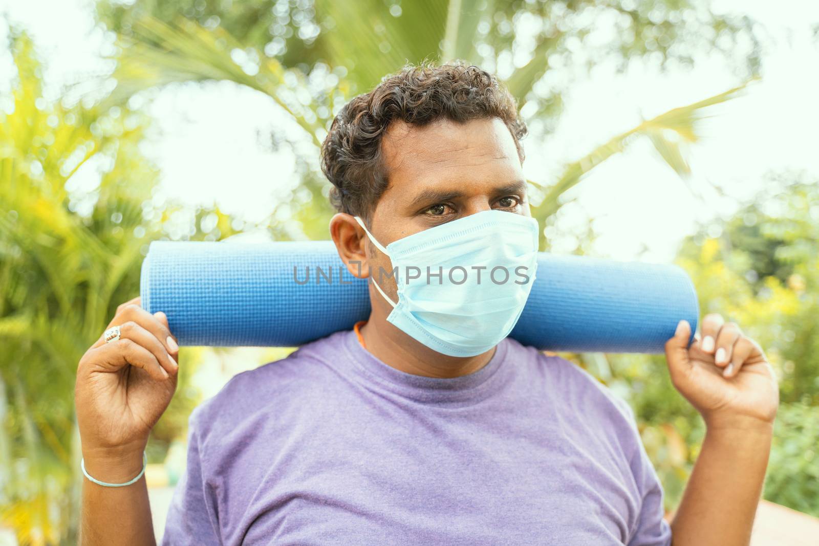 Fat man wearing medical face mask holding yoga mat on shoulder came for exercise after quarantine to park - concept of life after coronavirus or covid-19 lockdown and new normal.