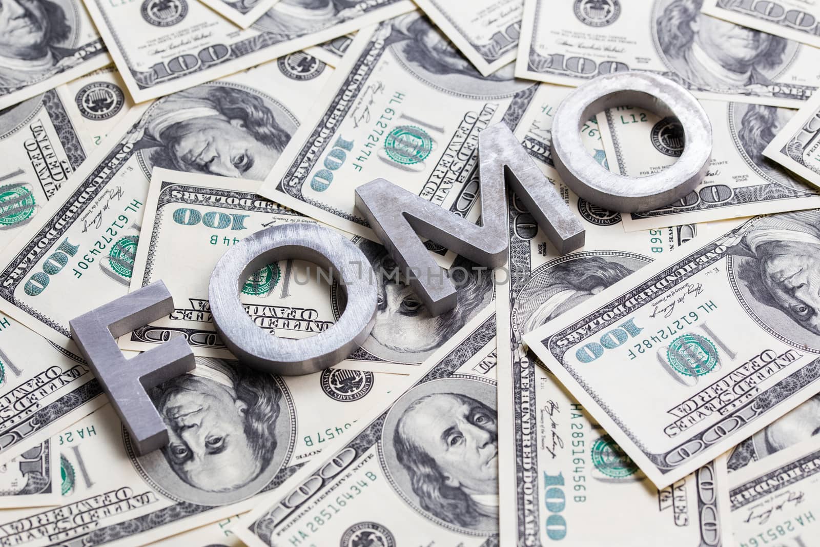 The word FOMO - fear of missing out - laid with aluminium letters on the US dollar banknotes background - with selective focus and diagonal composition.