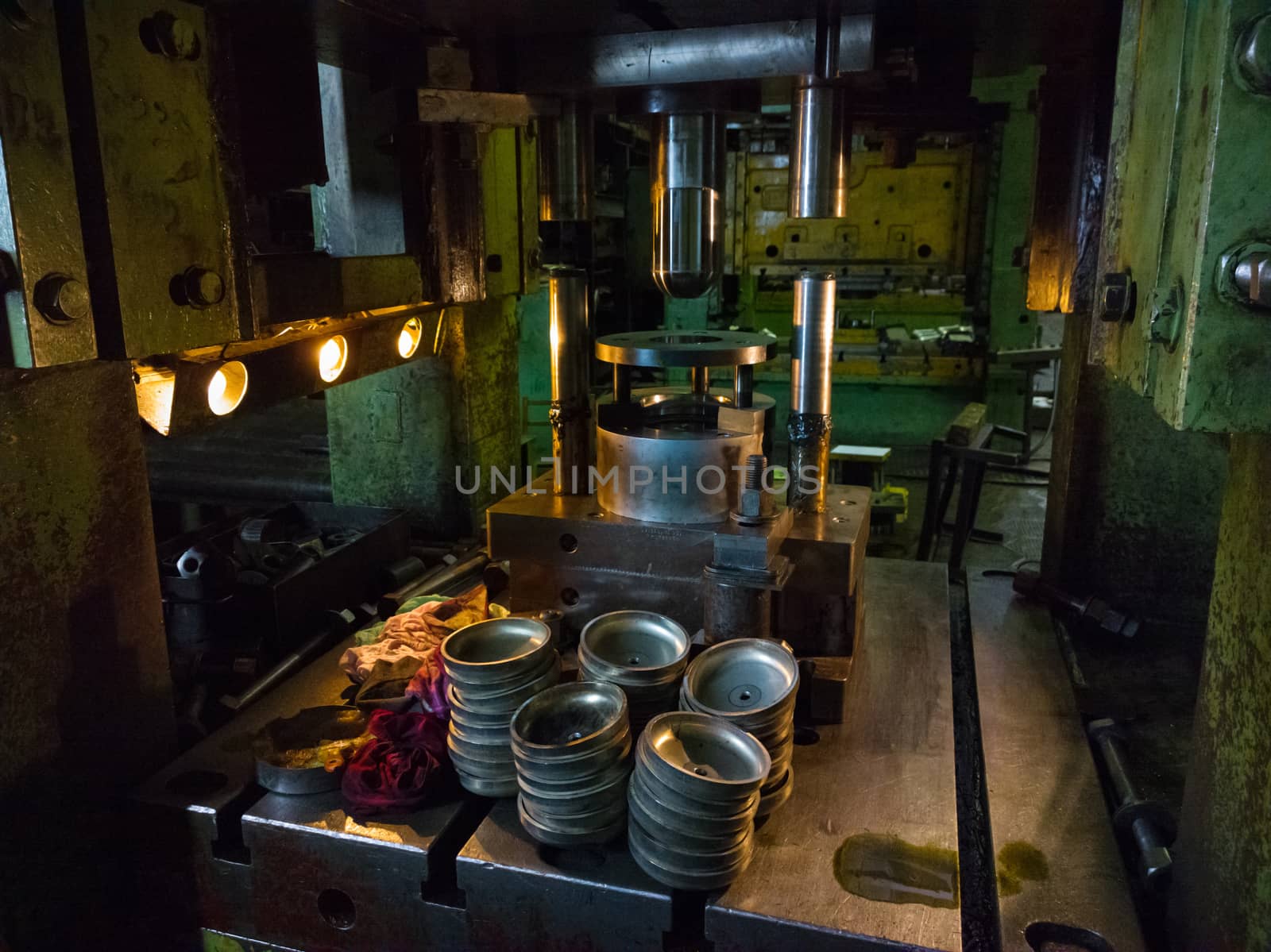 dirty used low tech stamping press producing round aliminium parts in dark environment.