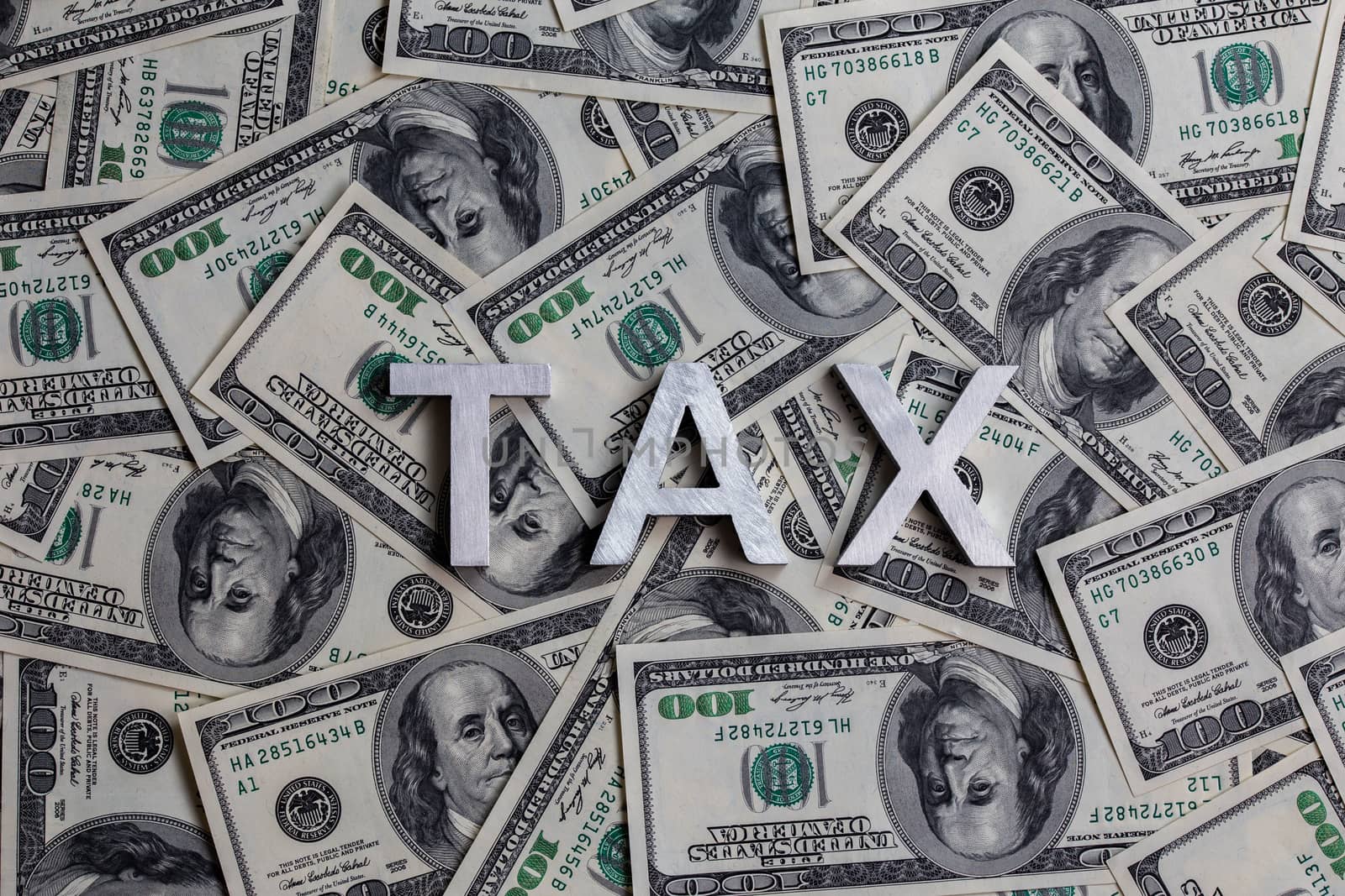 The words TAX laid with metal letters on the US dollar bills background - with selective focus and diagonal composition.