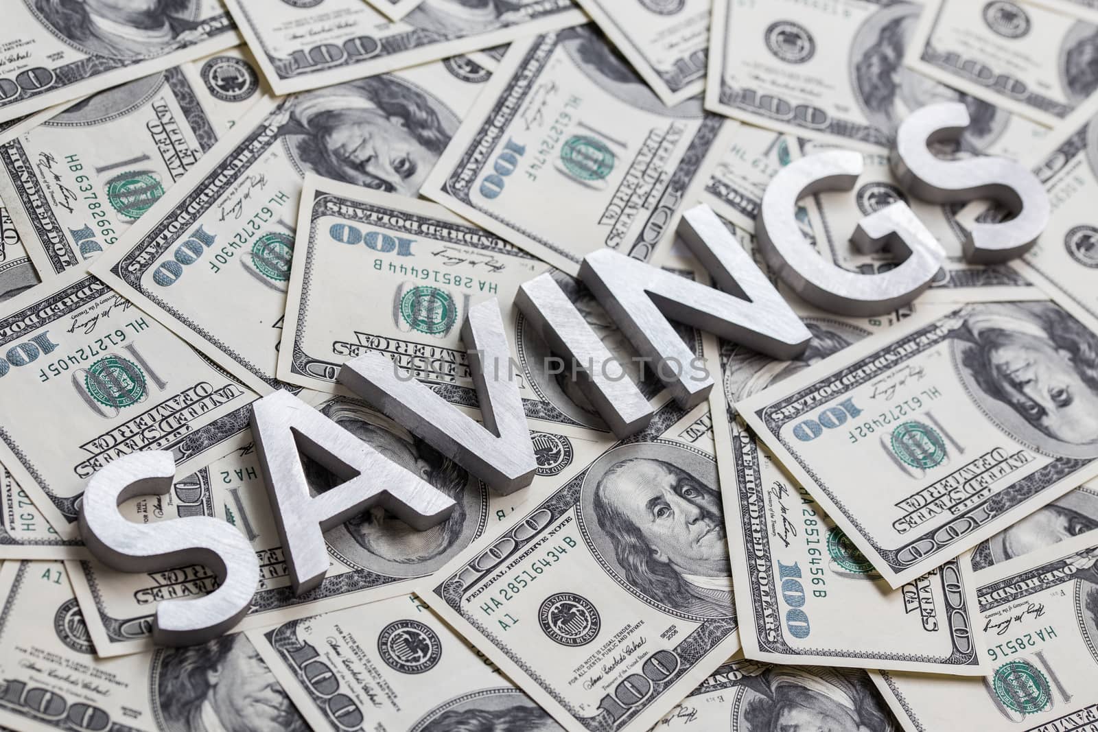 The word SAVINGS laid with white metal letters on the US banknotes background - with selective focus and diagonal composition.