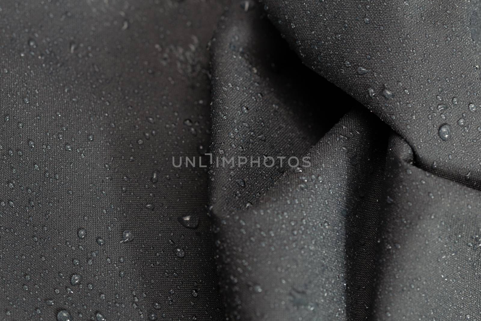 dark gray waterproof hydrophobic crumpled cloth closeup with water drops selective focus background.