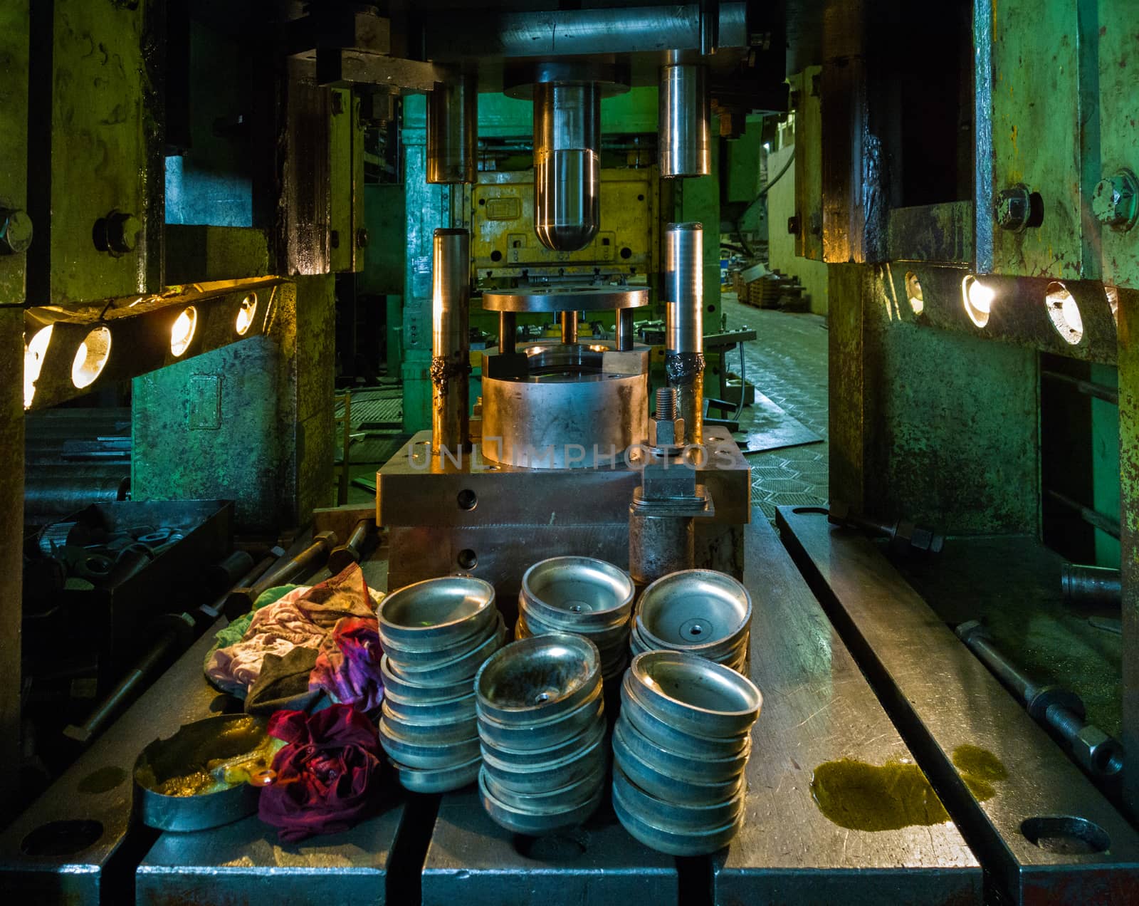 dirty used low tech stamping press producing round aliminium parts in dark environment.