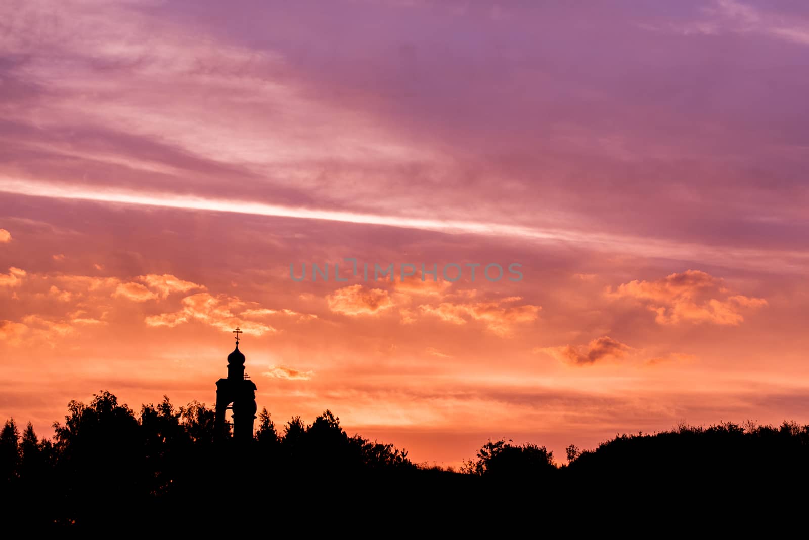 black silhouette of church and forest horizon on golden-purple sunset sky with soft clouds.