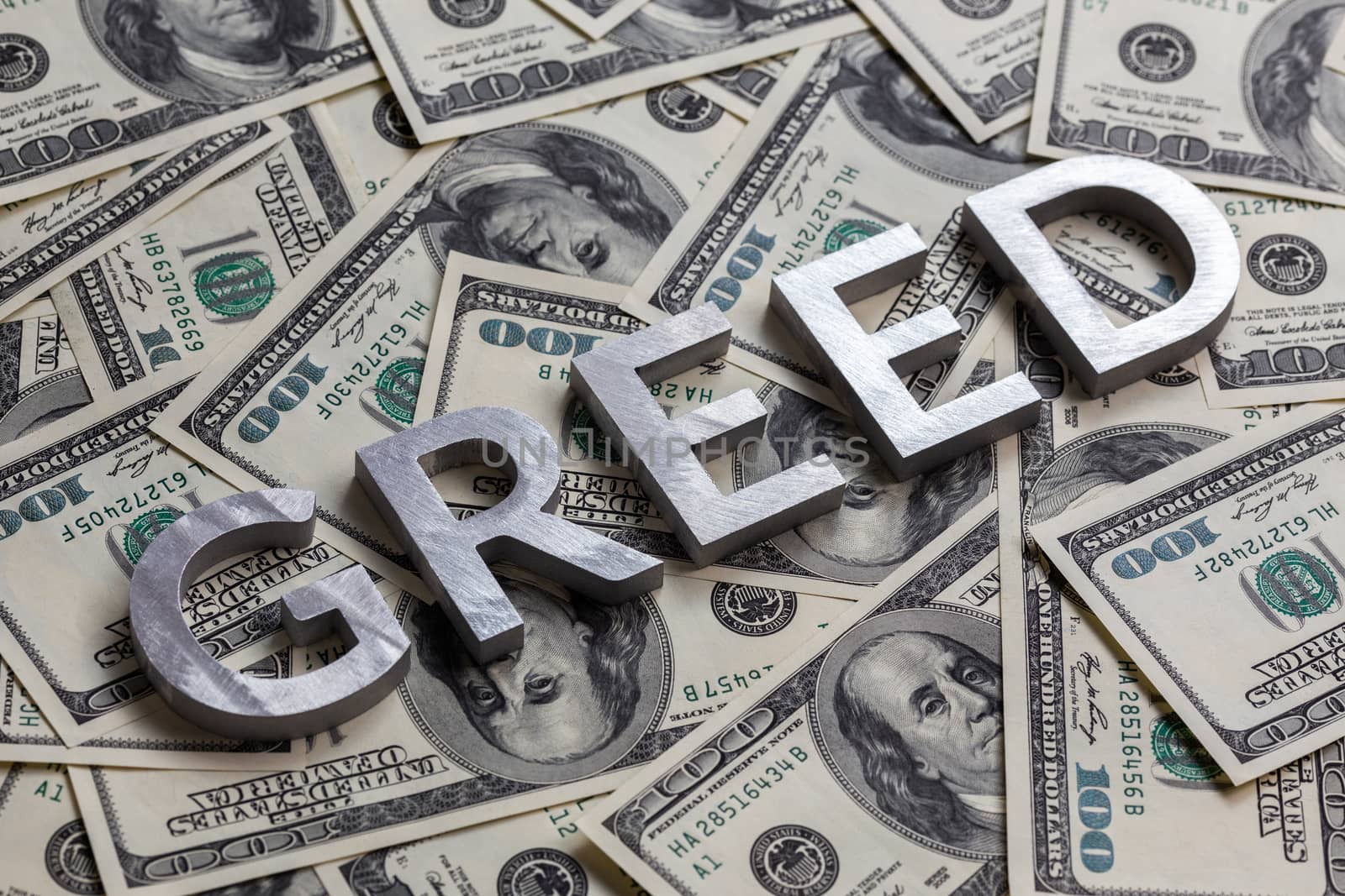 The word GREED laid with aluminium letters on the US dollar banknotes background - with selective focus and diagonal composition.