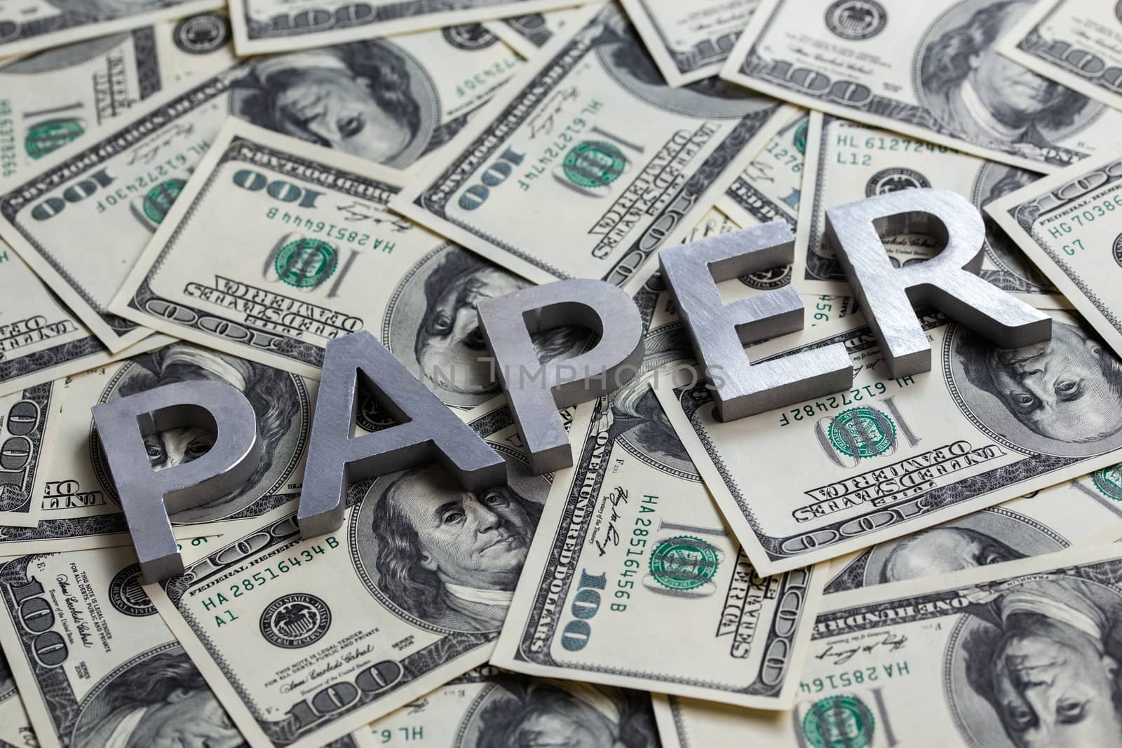 The word PAPER laid with aluminium letters on the US dollar banknotes background - with selective focus.