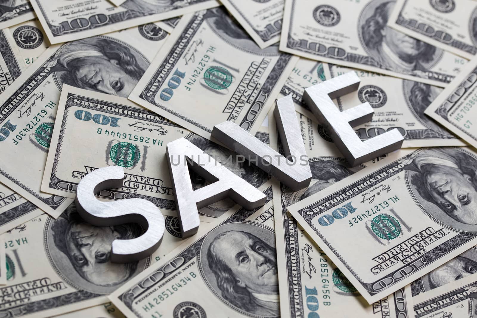 The word SAVE laid with white metal letters on the US banknotes background - with selective focus and diagonal composition.