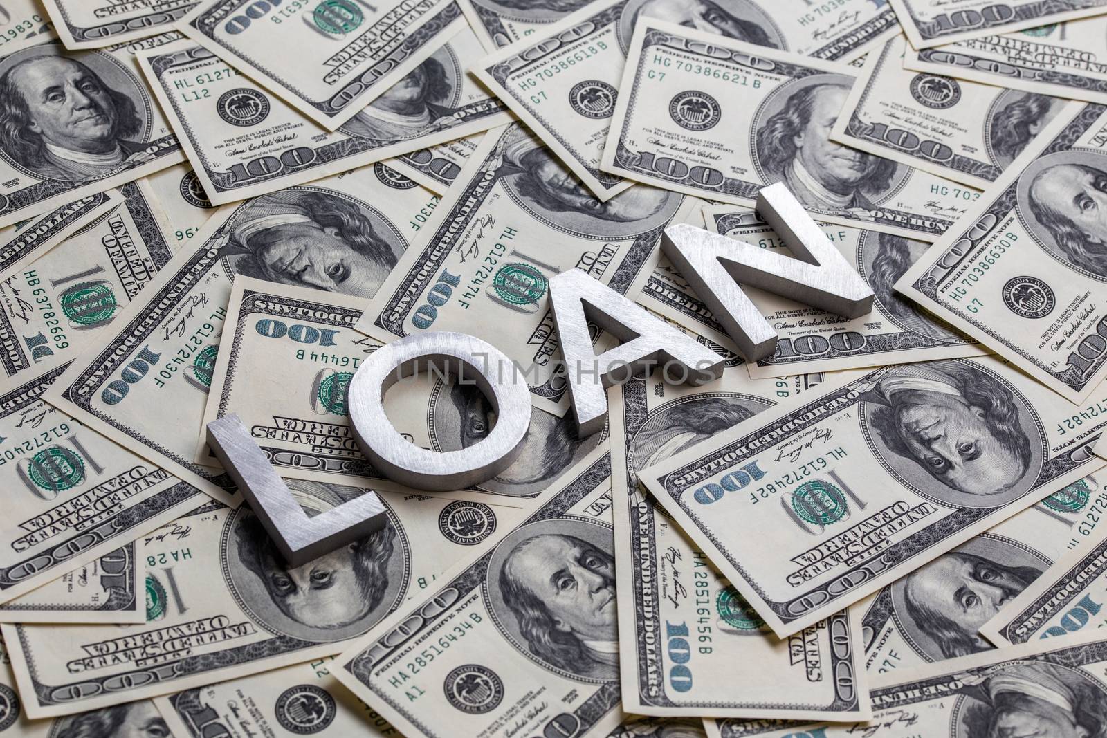 The word LOAN laid with aluminium letters on the US dollar banknotes background - with selective focus and diagonal composition.