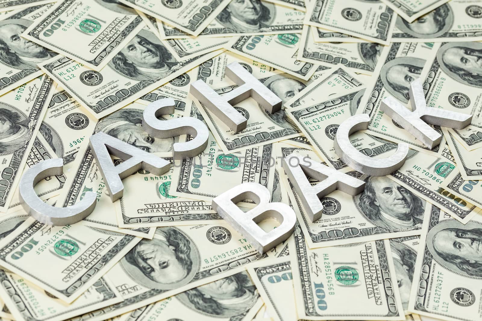 The words CASH BACK laid with aluminium thick letters on the US dollar bills background - with selective focus and diagonal composition.