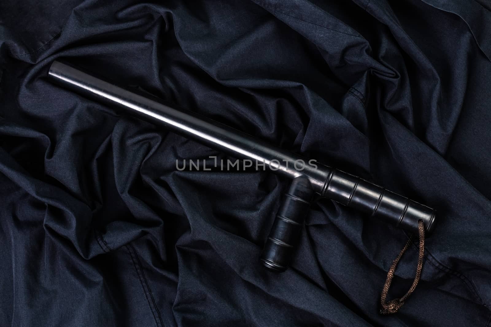 black rubber police baton on black shirt wrinkled cloth low-key flat lay.