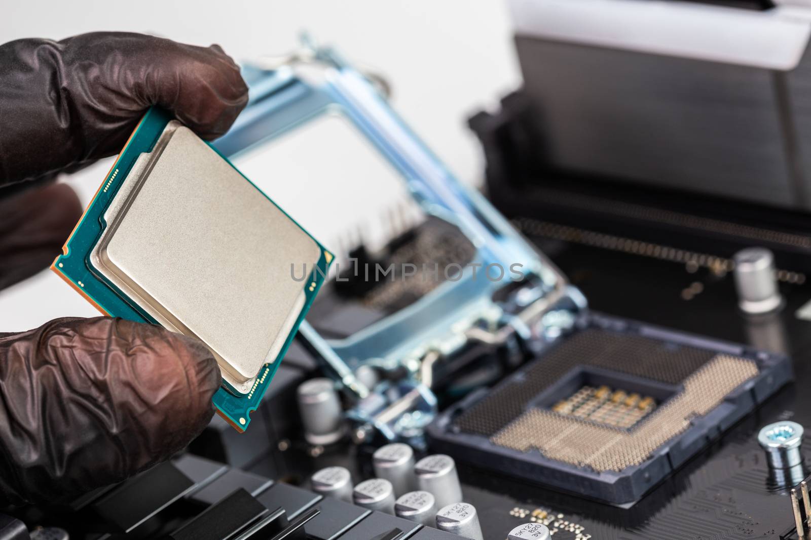 hand in black plastic glove holding central processor unit before installation on blurry opened socket on mainboard background