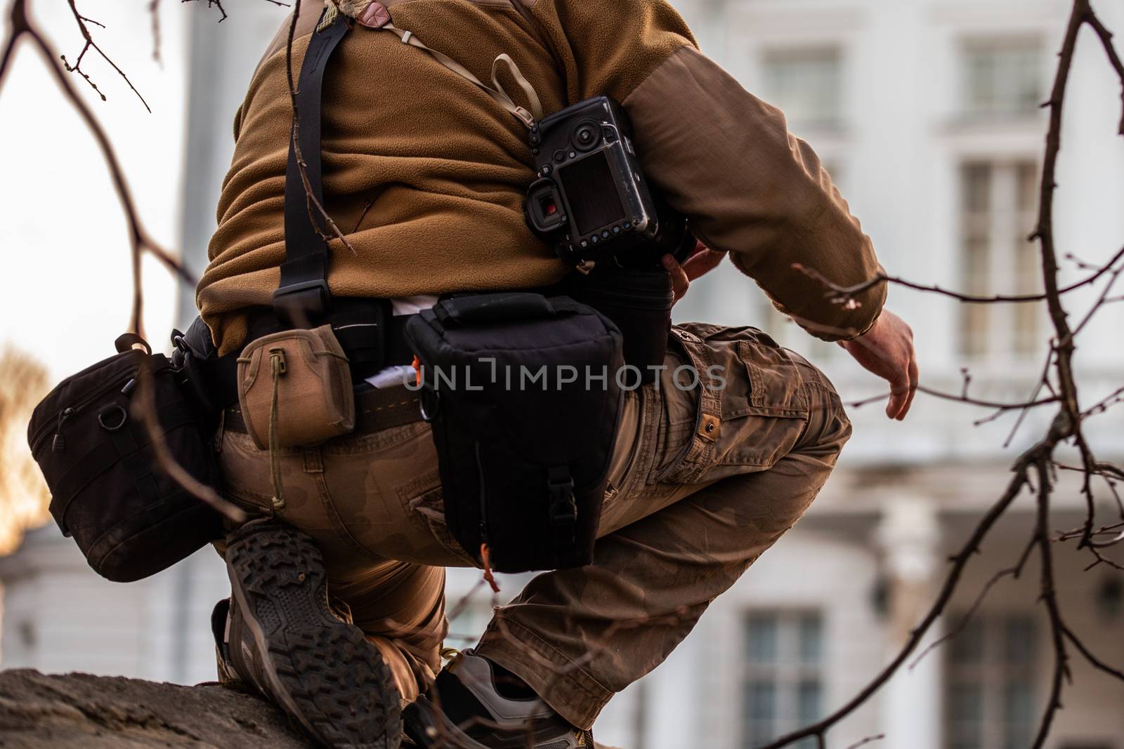 Professional extreme photographer belt pouch system gear in action. Sneaky photoshoot on the fence of private white building.