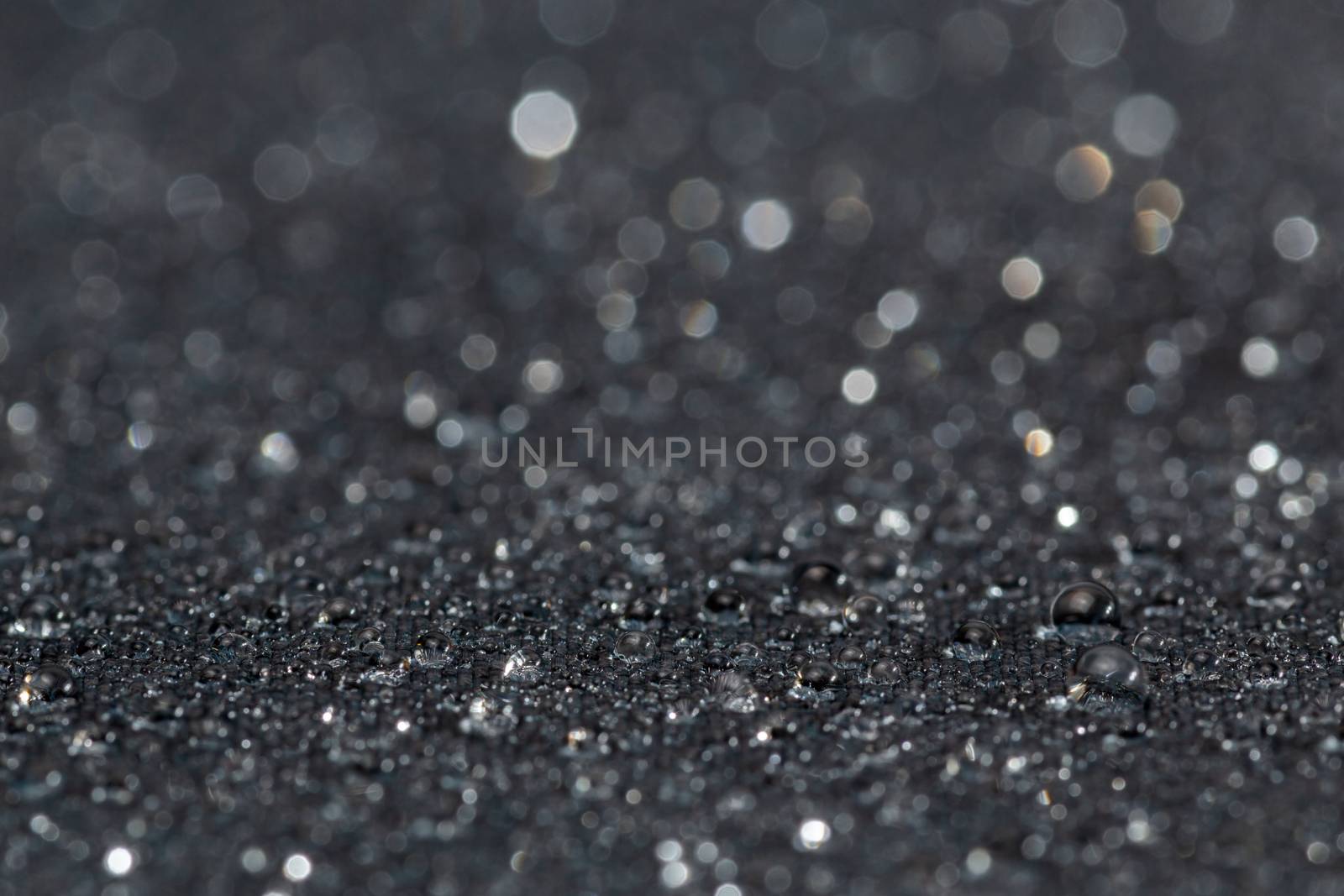 dark grey water resistant hydrophobic flat cloth with rain drops, close-up background with selective focus and bokeh blur