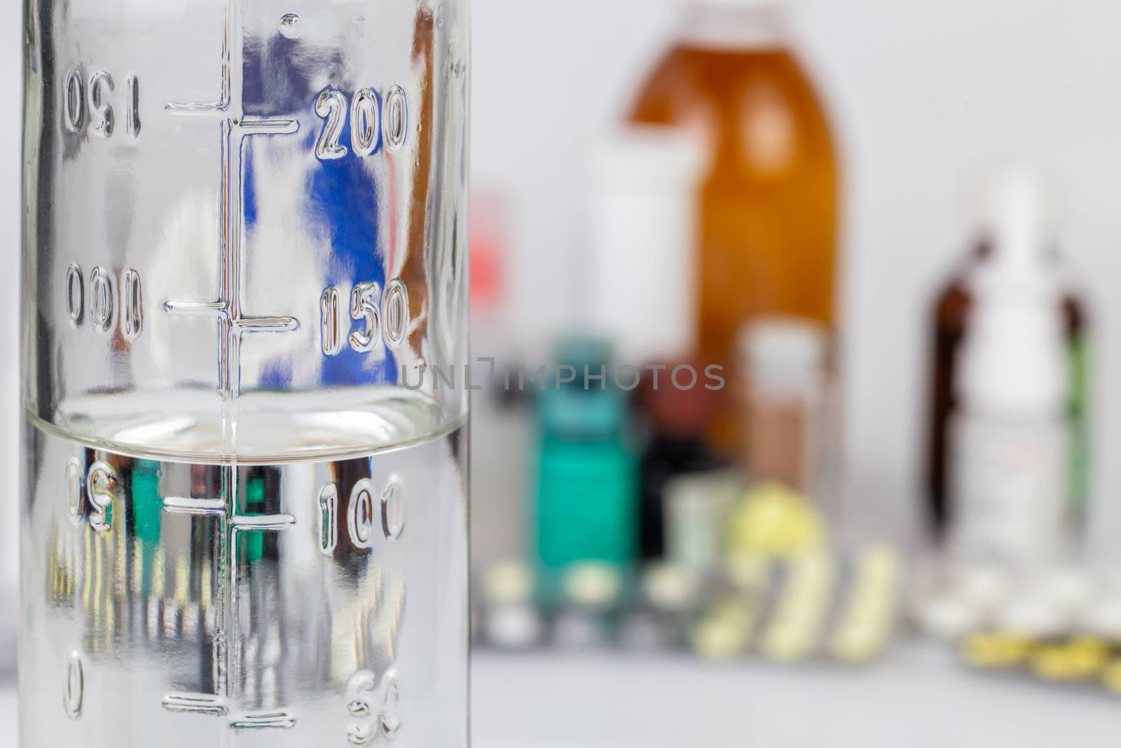 measuring bottle glass bottle with colorless liquid on blurred meds background with selective focus.