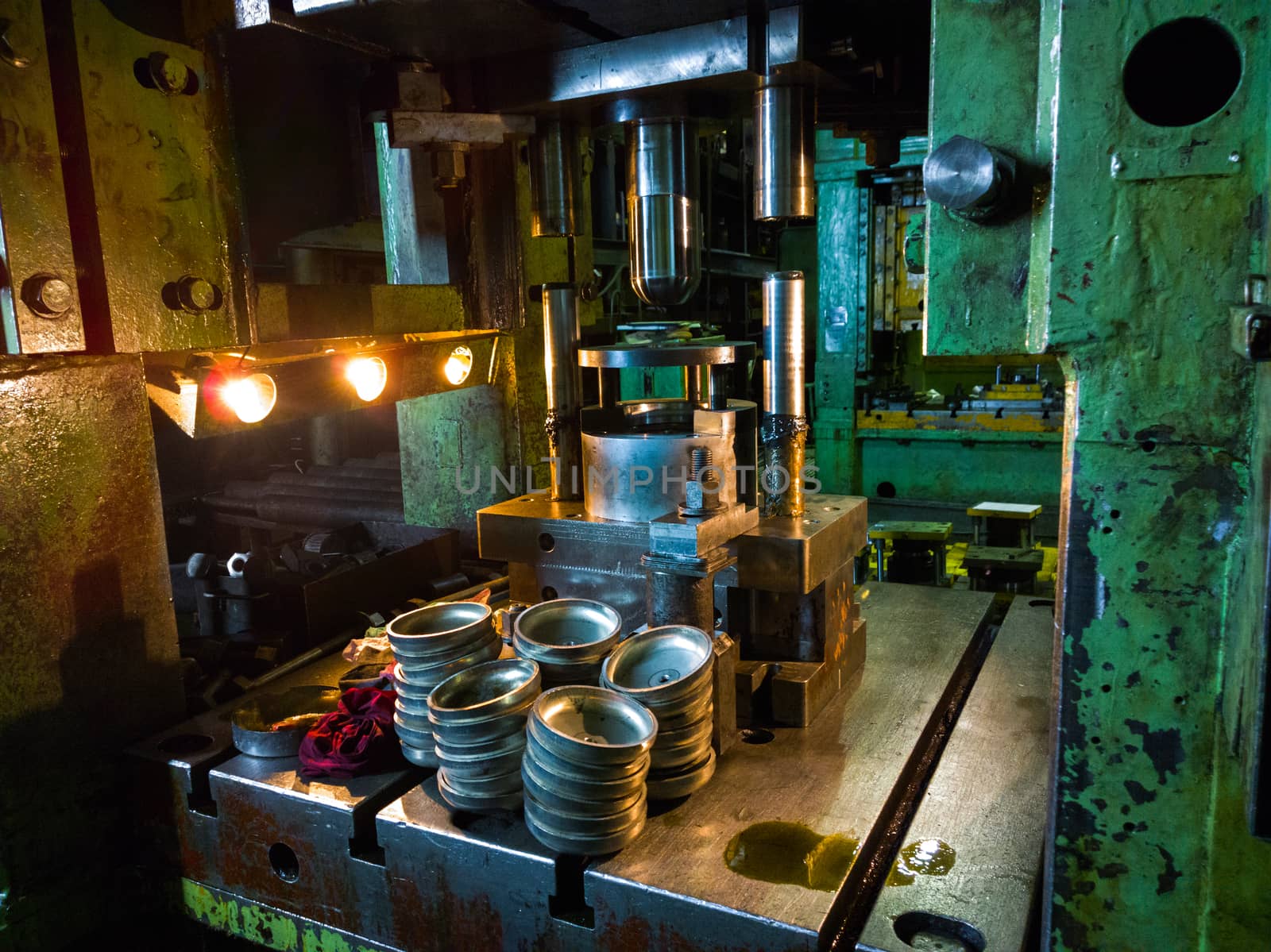 dirty used low tech stamping press producing round aliminium parts in dark environment.