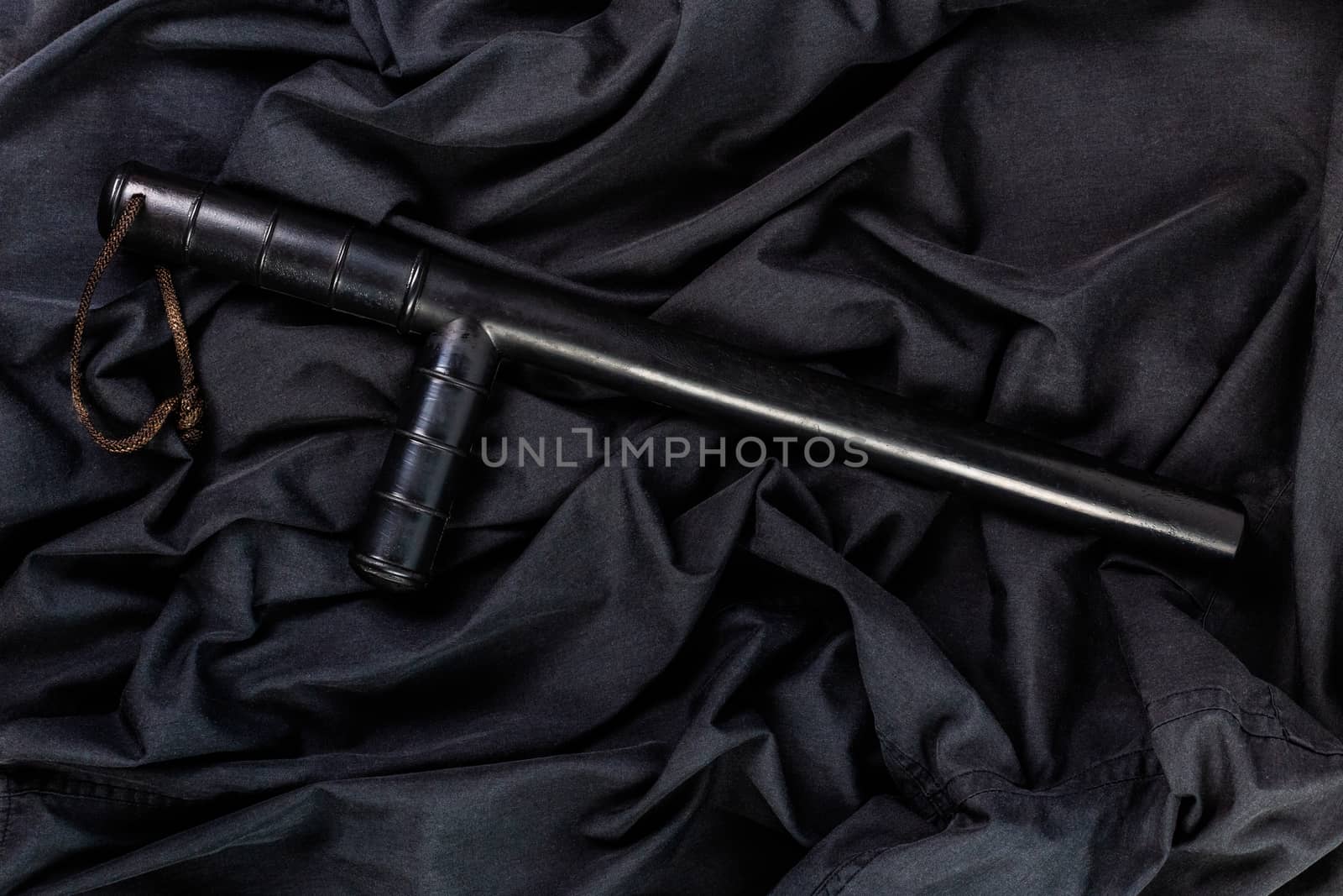 black rubber police baton on black shirt wrinkled cloth low-key flat lay.