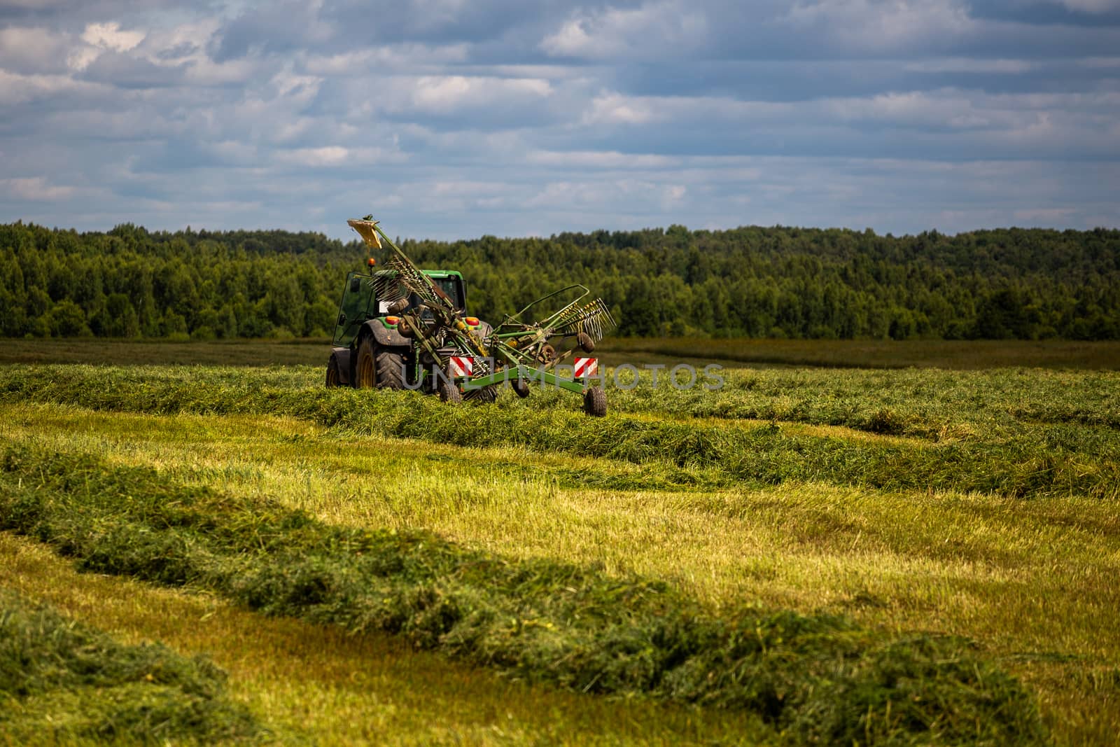 green haymaking tractor on summer field before storm - telephoto shot with selective focus and blur.