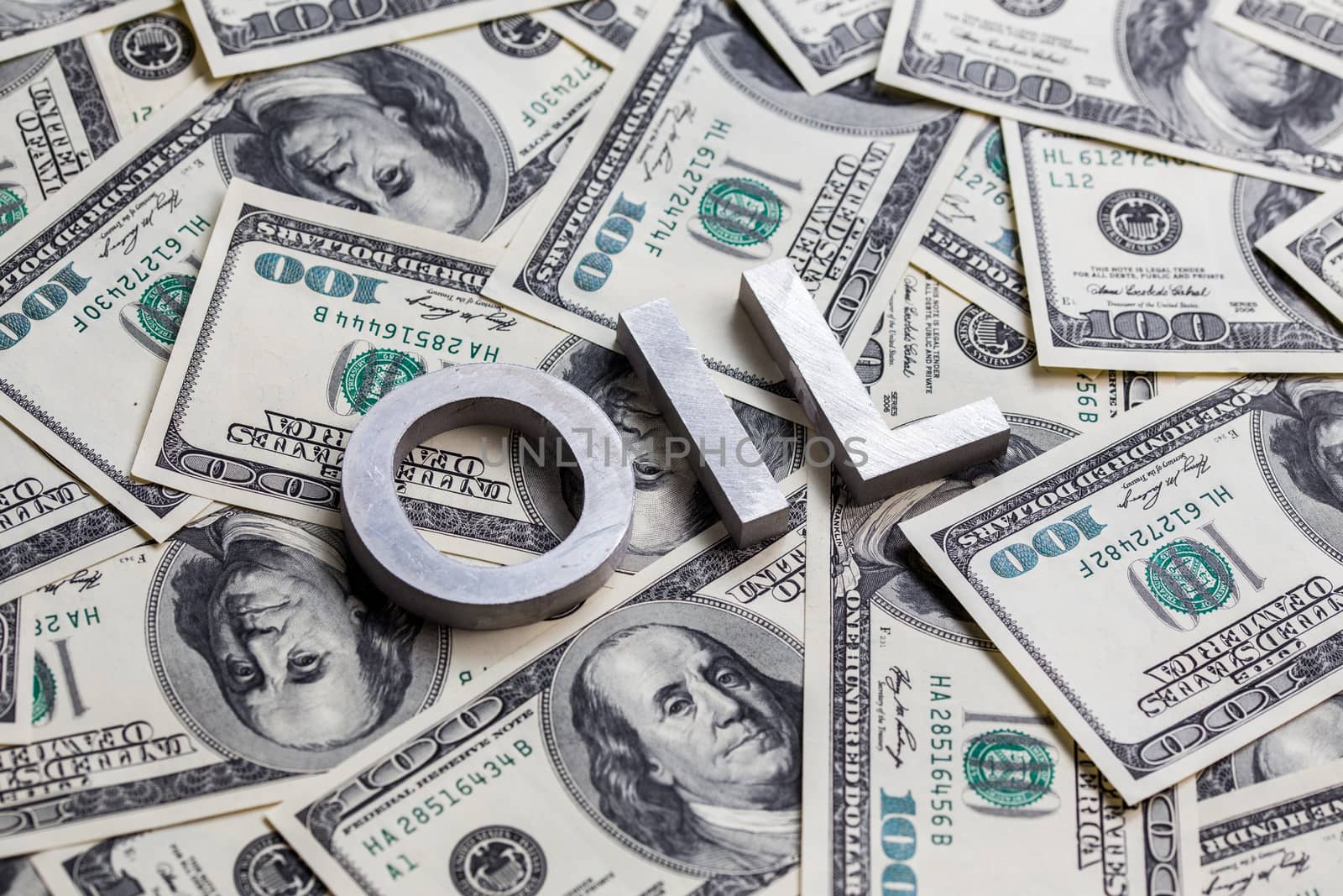The word OIL laid with aluminium letters on the US dollar banknotes background - with selective focus and diagonal composition.