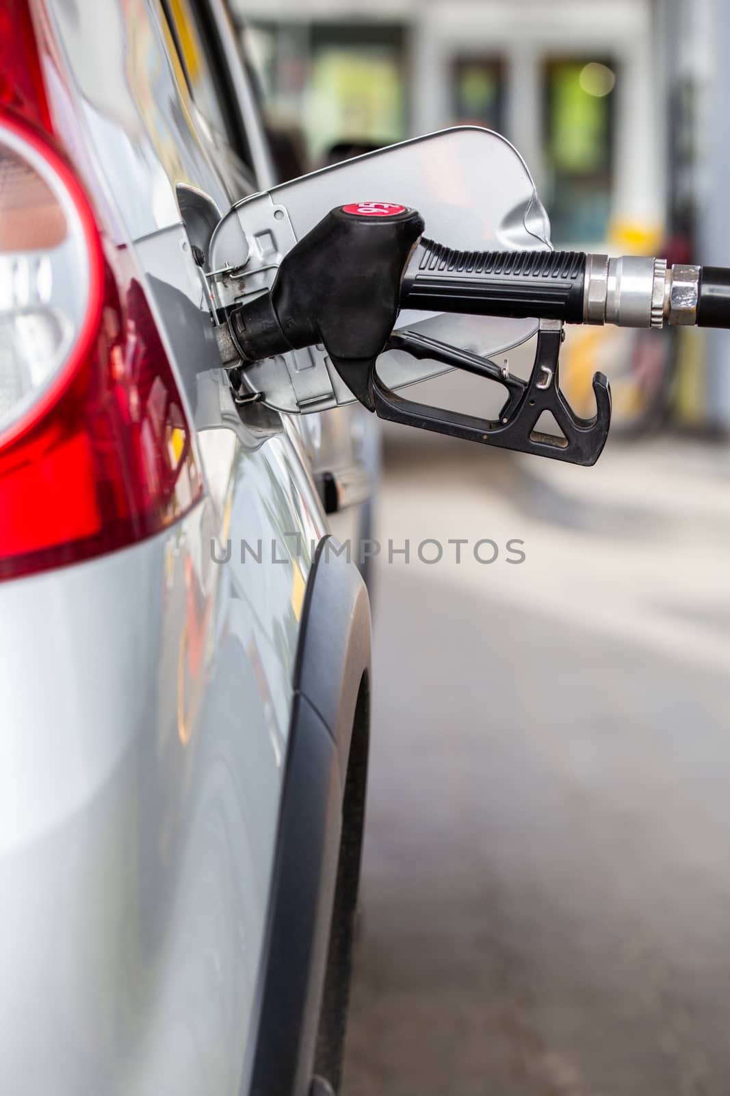 gray metallic car refueling on gas station - closeup with selective focus and blurry man on background. Vertical composition.