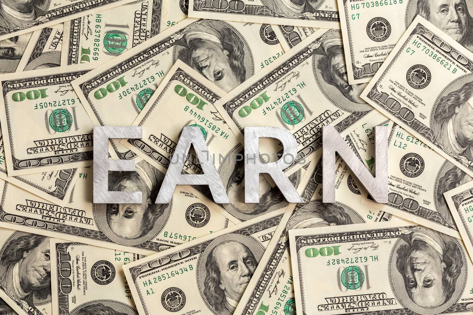 The word earn laid with aluminium letters on the US dollar banknotes background - with selective focus and diagonal composition.